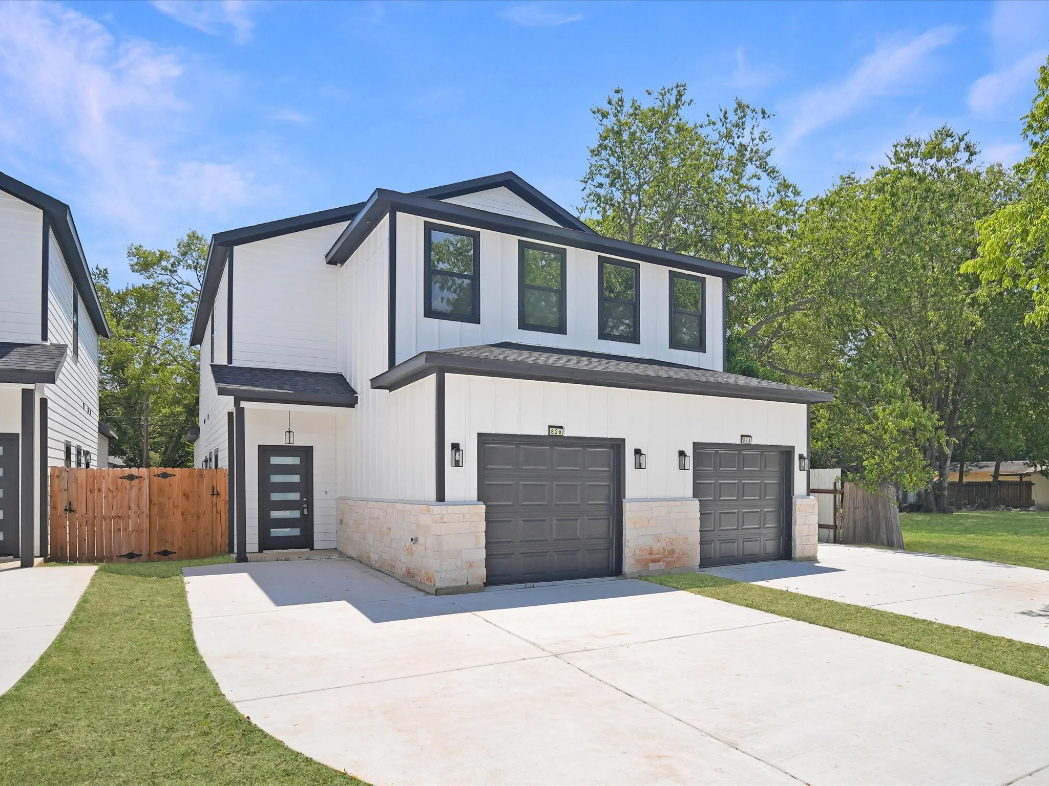 Modern exterior with white vertical siding, black trim accents, a dark entry door, two garage bays, and a stone-clad base