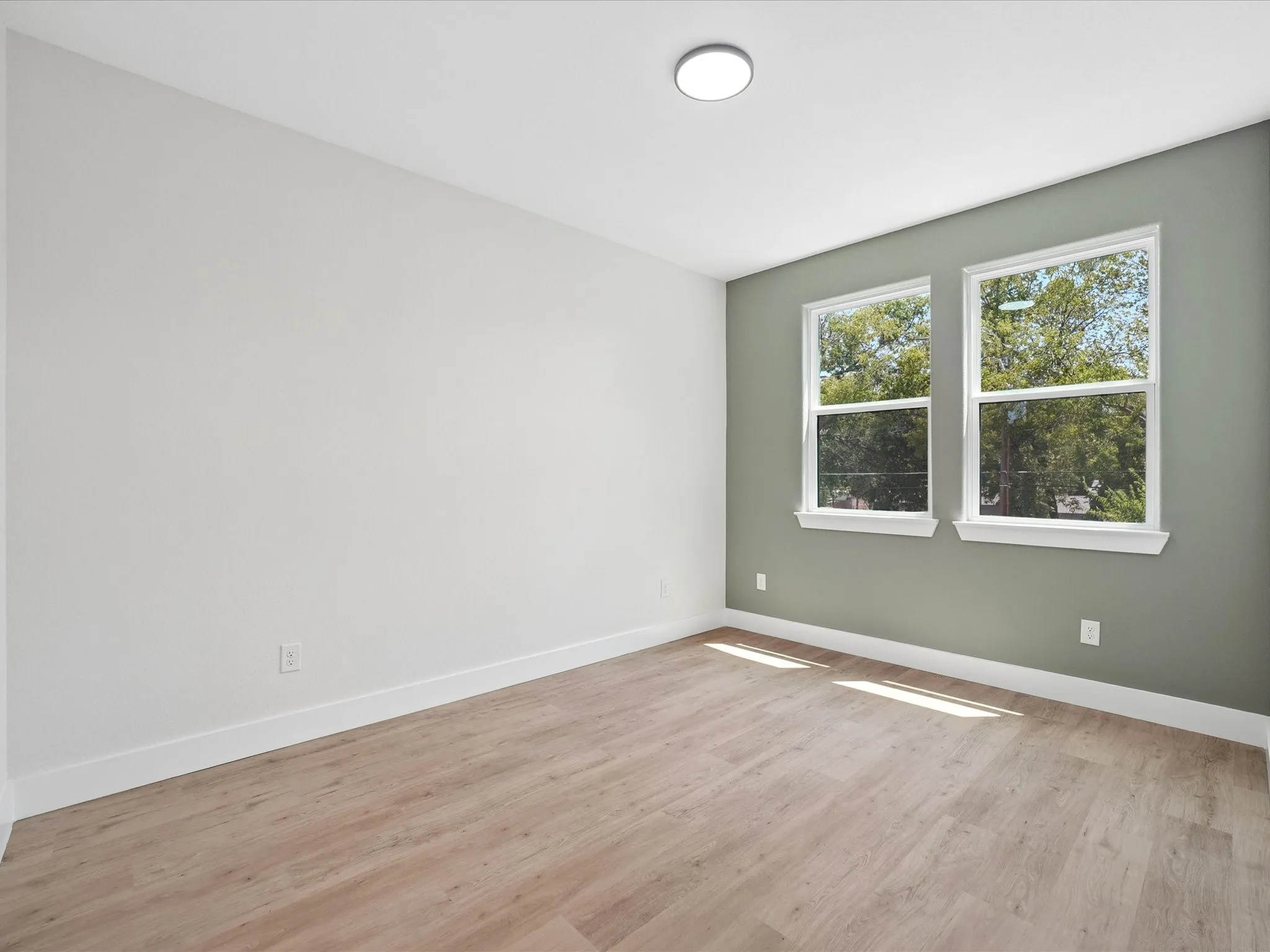 Wood-finish flooring, dual windows with white trim, a flush-mount ceiling light, and two-tone wall finishes