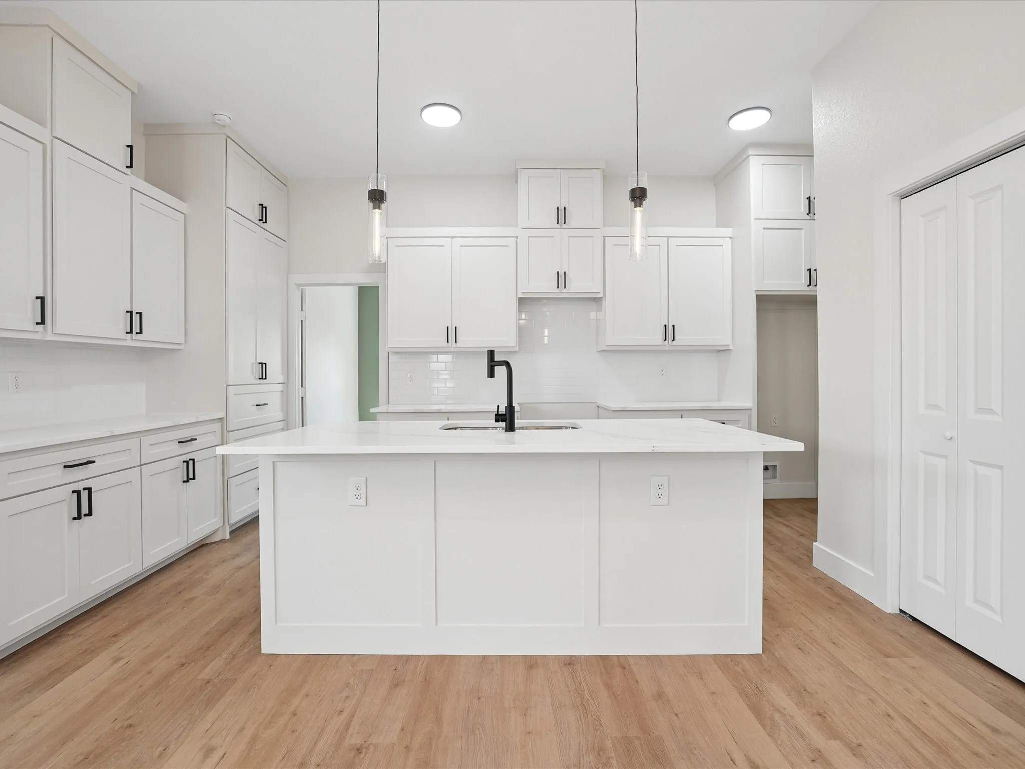 White shaker cabinetry with black hardware, white countertops, wood-finish flooring, and a central island with pendant lighting