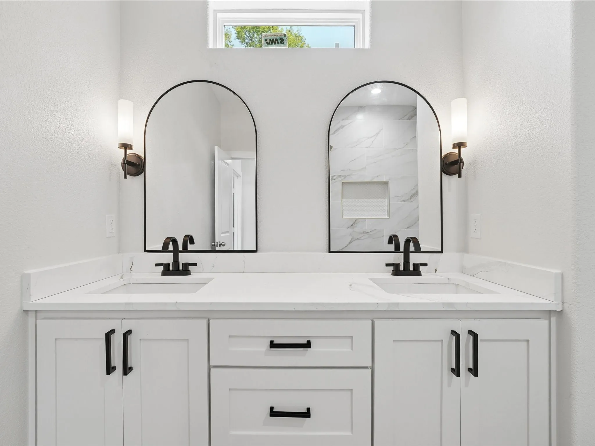 Dual vanity with white cabinetry and black hardware, stone-finish countertops, undermount sinks, and arched mirrors