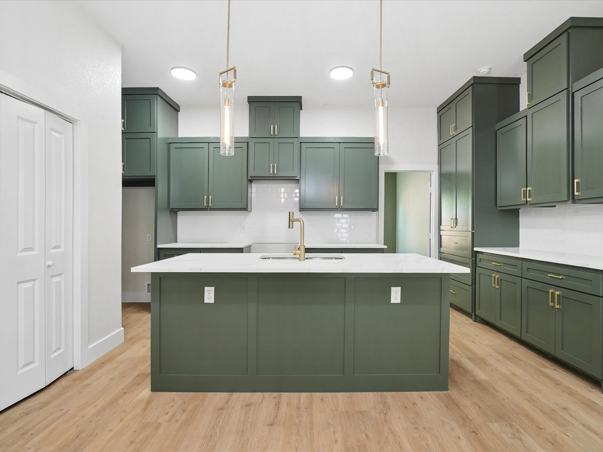 Kitchen featuring extensive green cabinetry, a central island with a sink, white countertops, wood-finish flooring, and pendant lighting fixtures