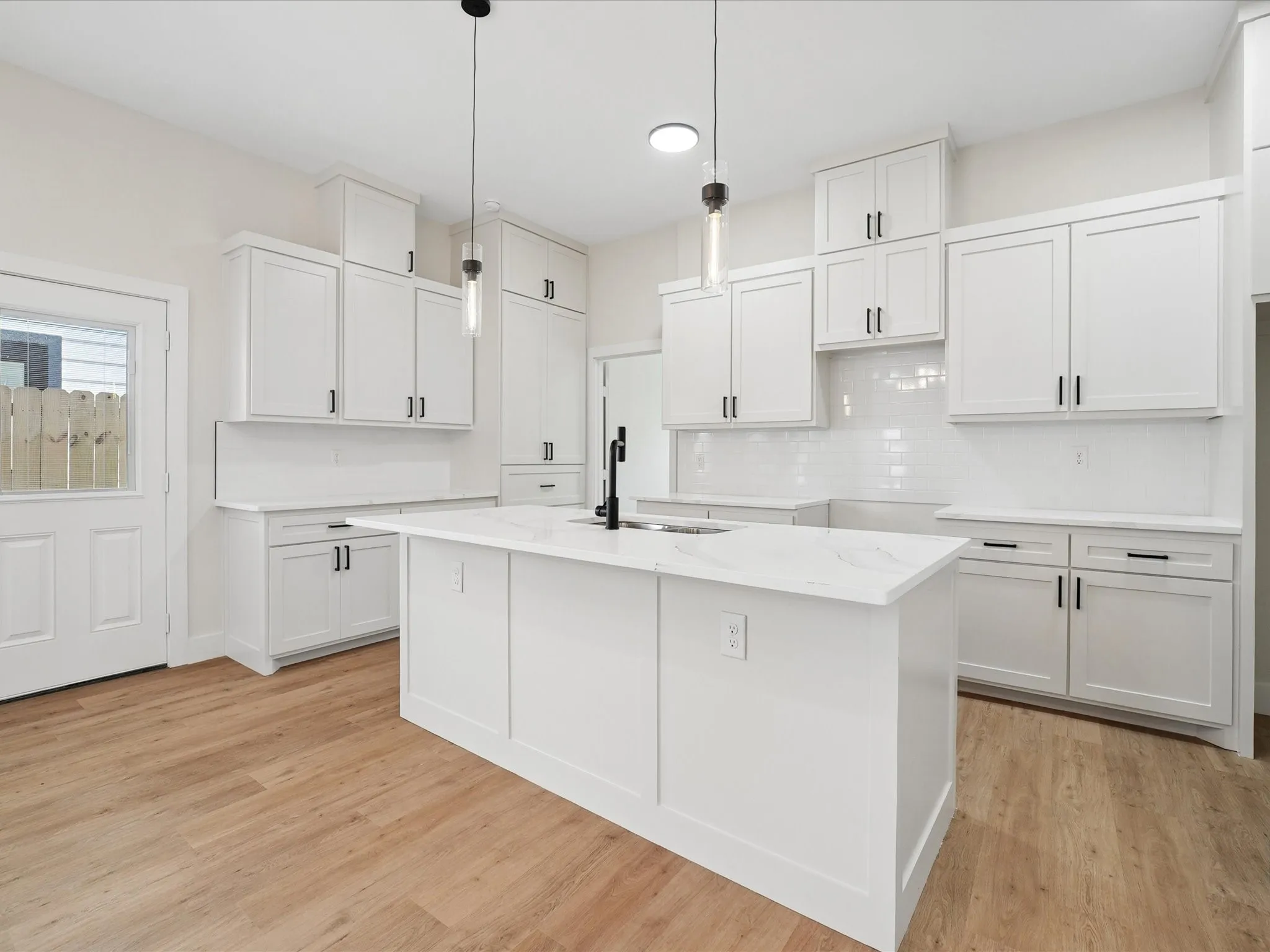 Kitchen featuring white shaker cabinetry, an expansive center island with a stone-finish countertop, wood-finish flooring, and subway tile backsplash