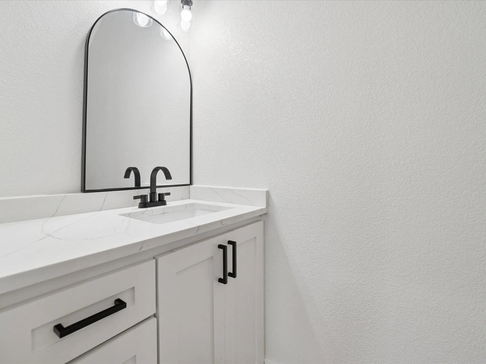 Arched mirror with black frame, white countertop with integrated sink, black faucet, and white cabinetry with black hardware