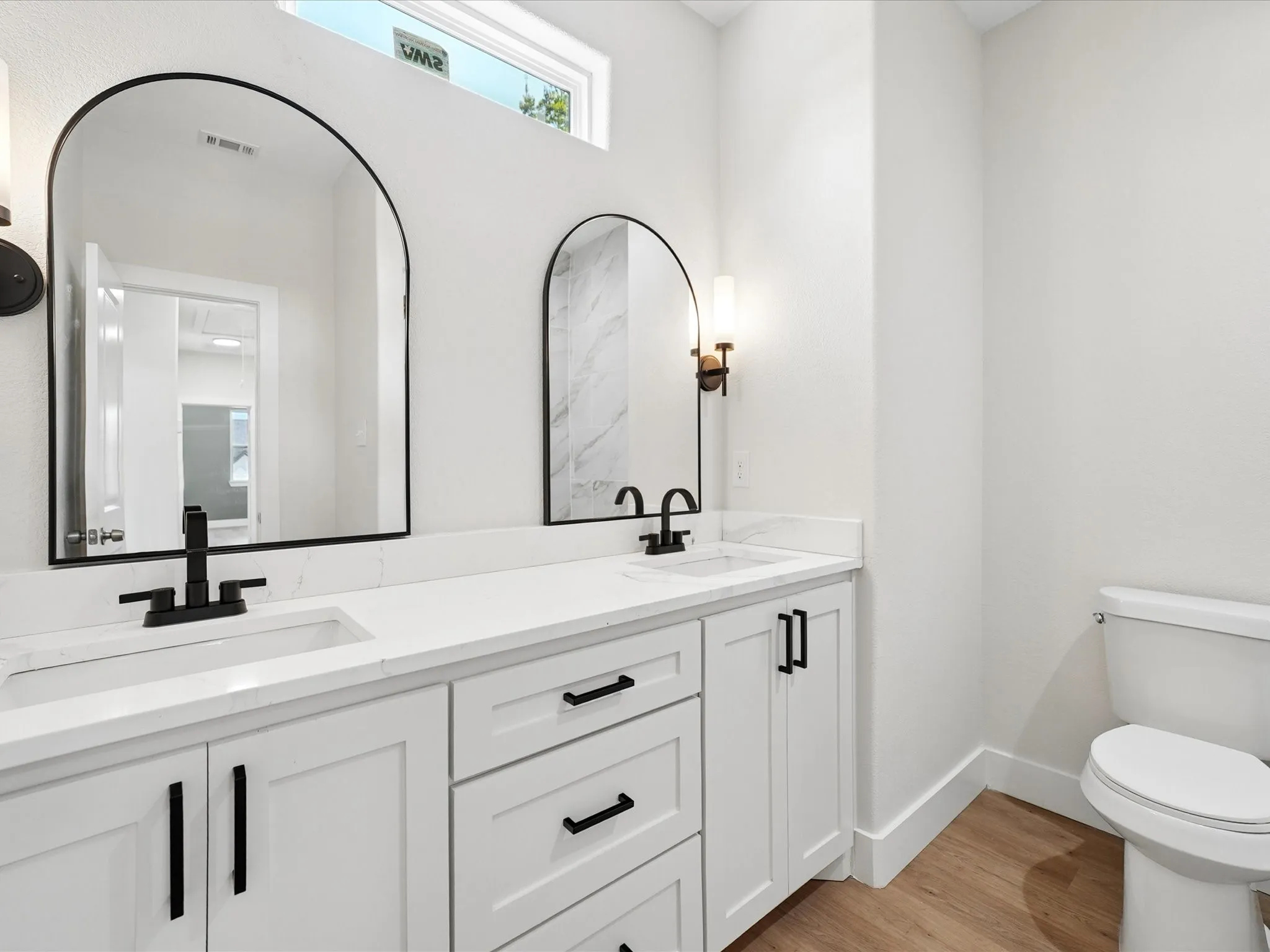 Dual vanity with white cabinetry, matte black hardware, white countertops, and arched mirrors