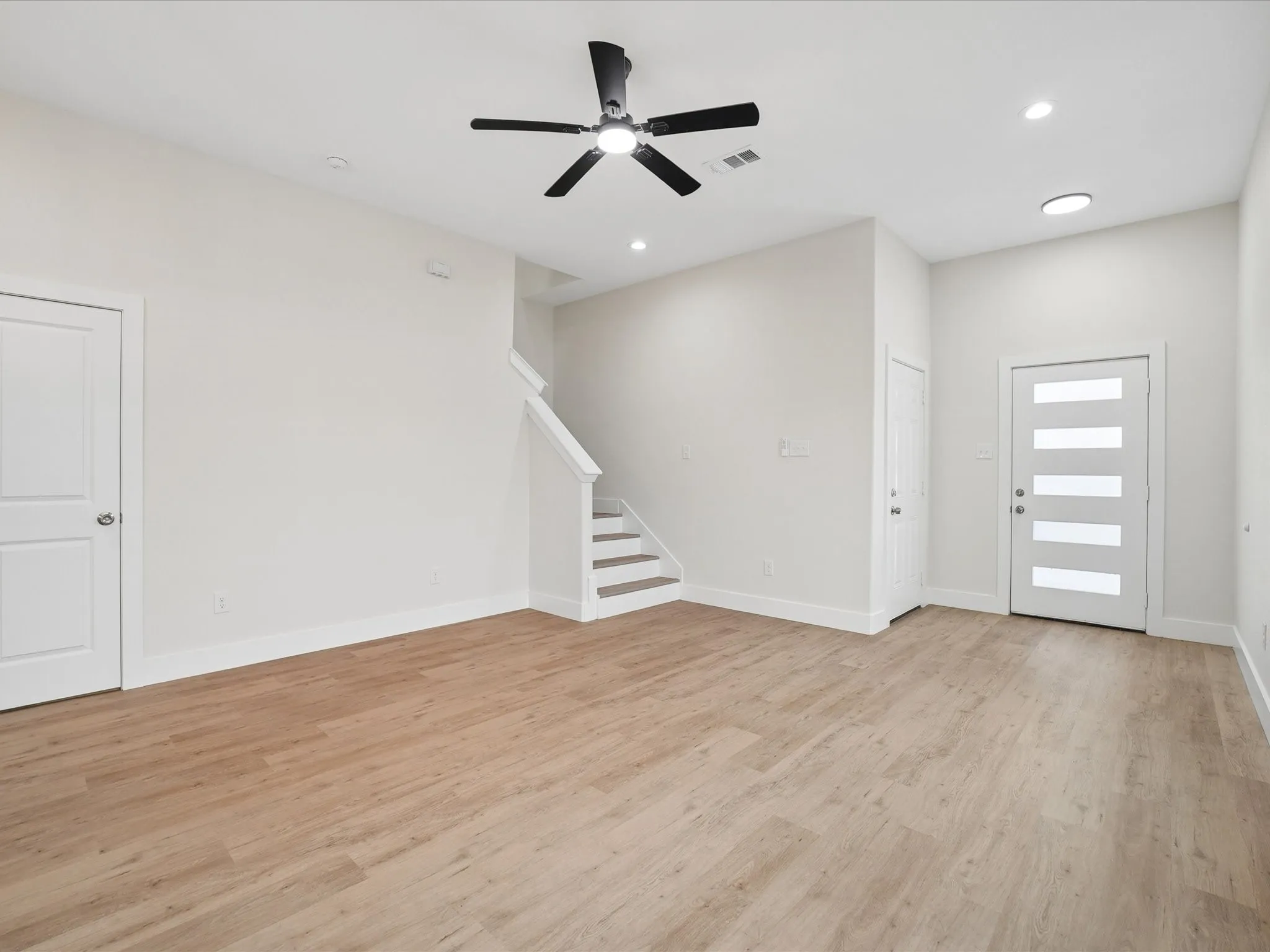 Wood-finish flooring, recessed lighting, ceiling fan, contemporary front door, and painted staircase