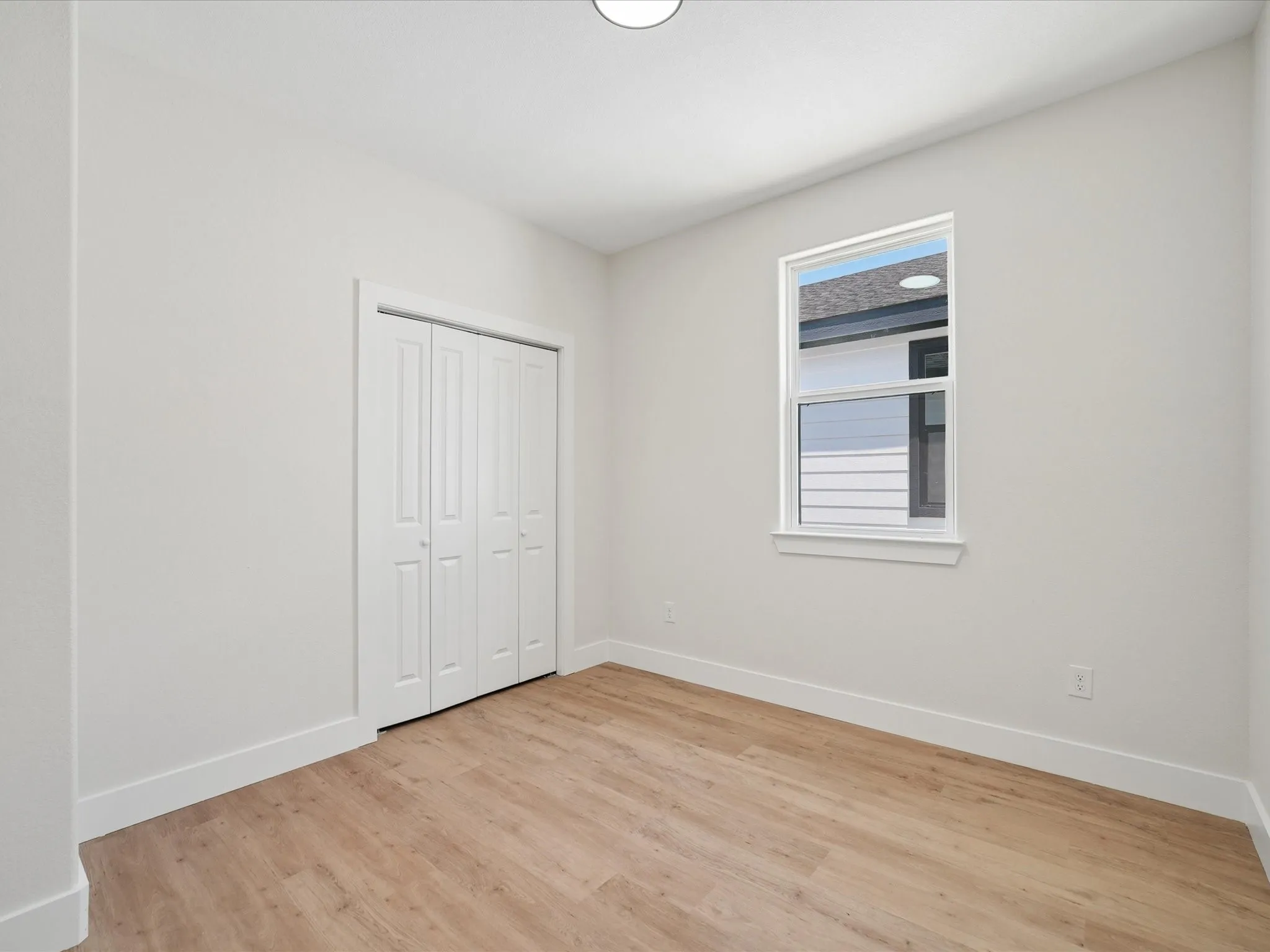 Recessed ceiling lighting, wood-finish flooring, white walls, white trim, and a white bi-fold closet door