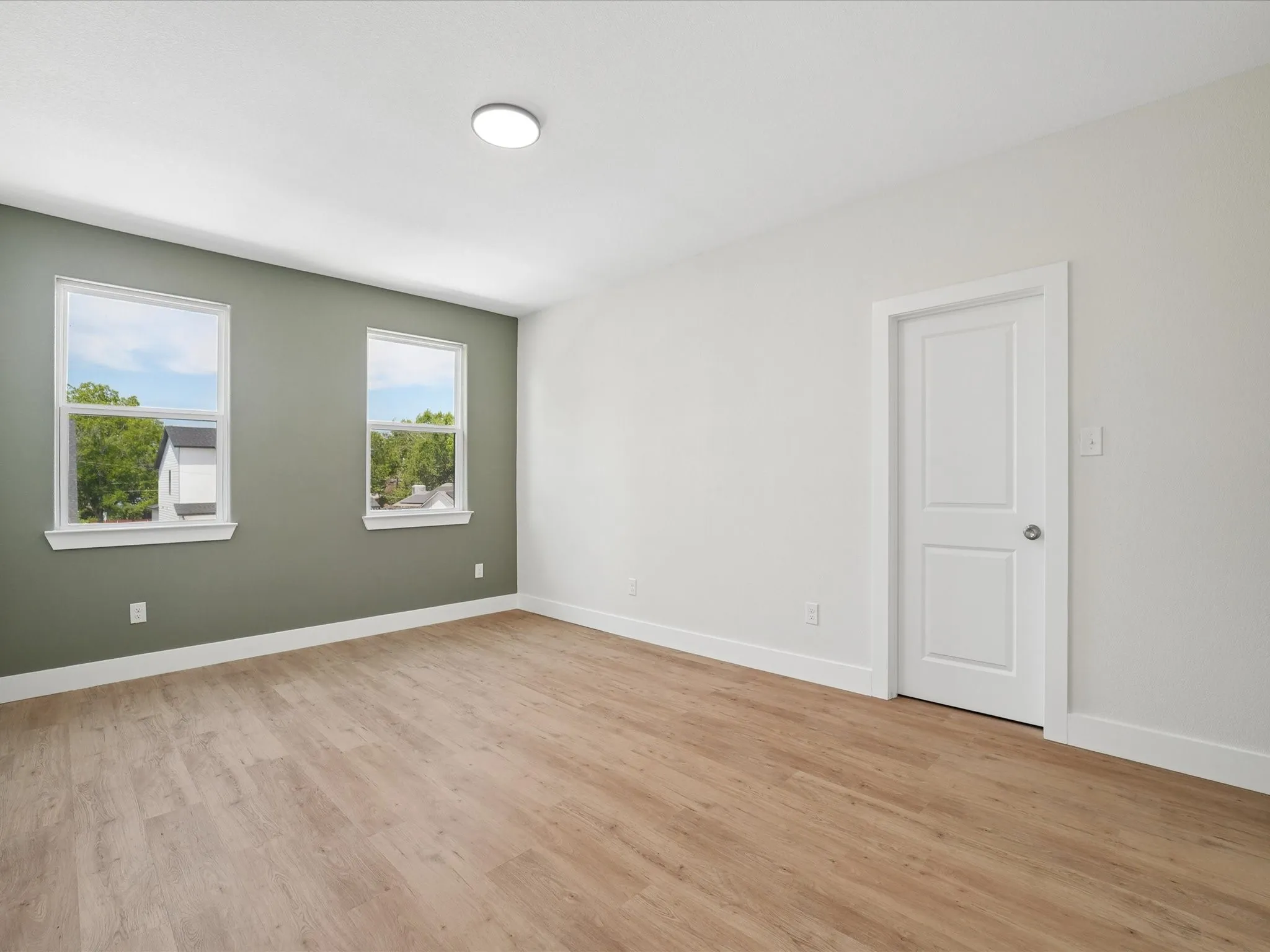 Recessed ceiling light fixture, wood-finish flooring, two large windows, white door, and white trim