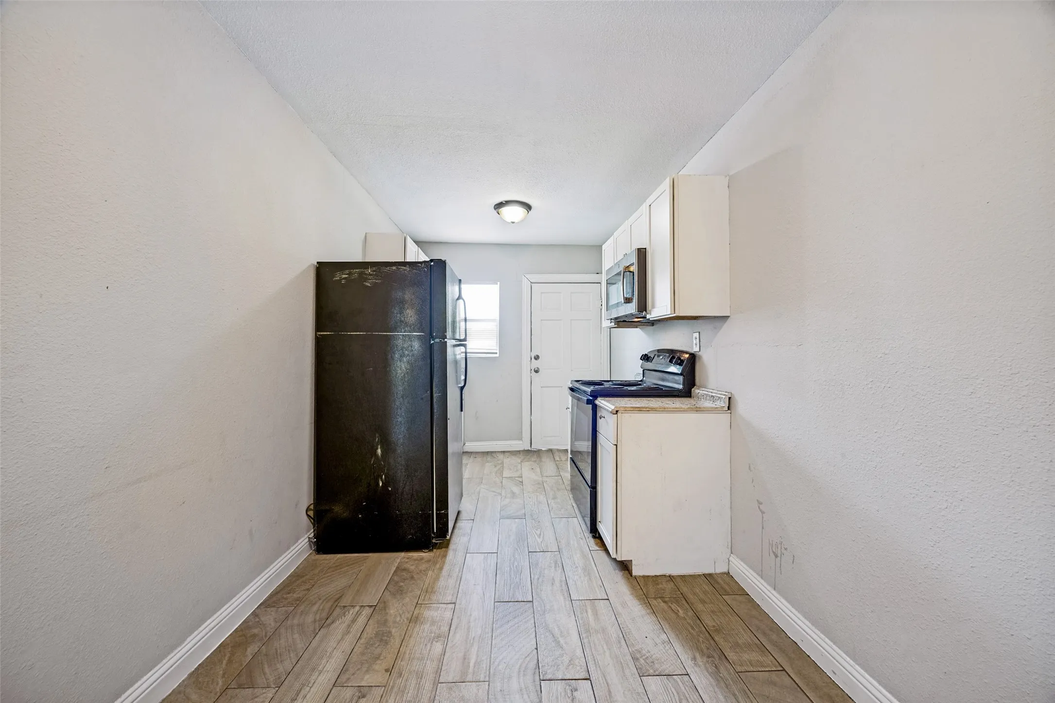 Wood-finish flooring with white baseboards, white upper and lower cabinetry, and a built-in microwave