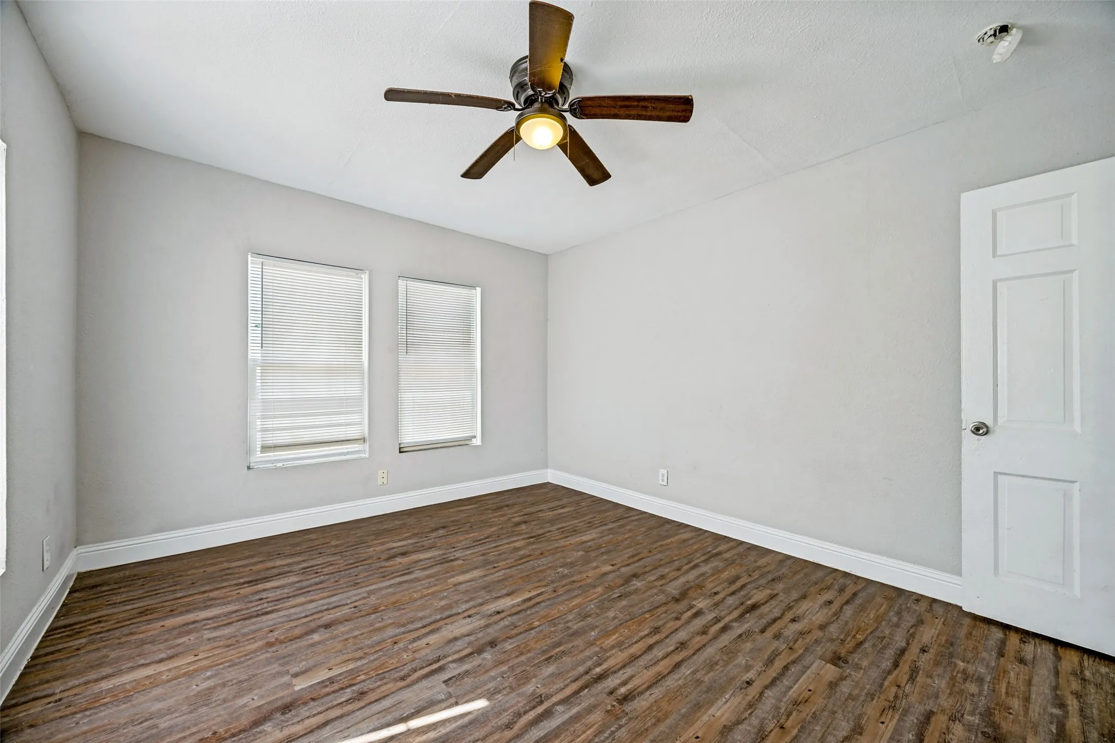 Sloped ceiling with an attached ceiling fan, wood-finish flooring, two windows with blinds, and a paneled interior door