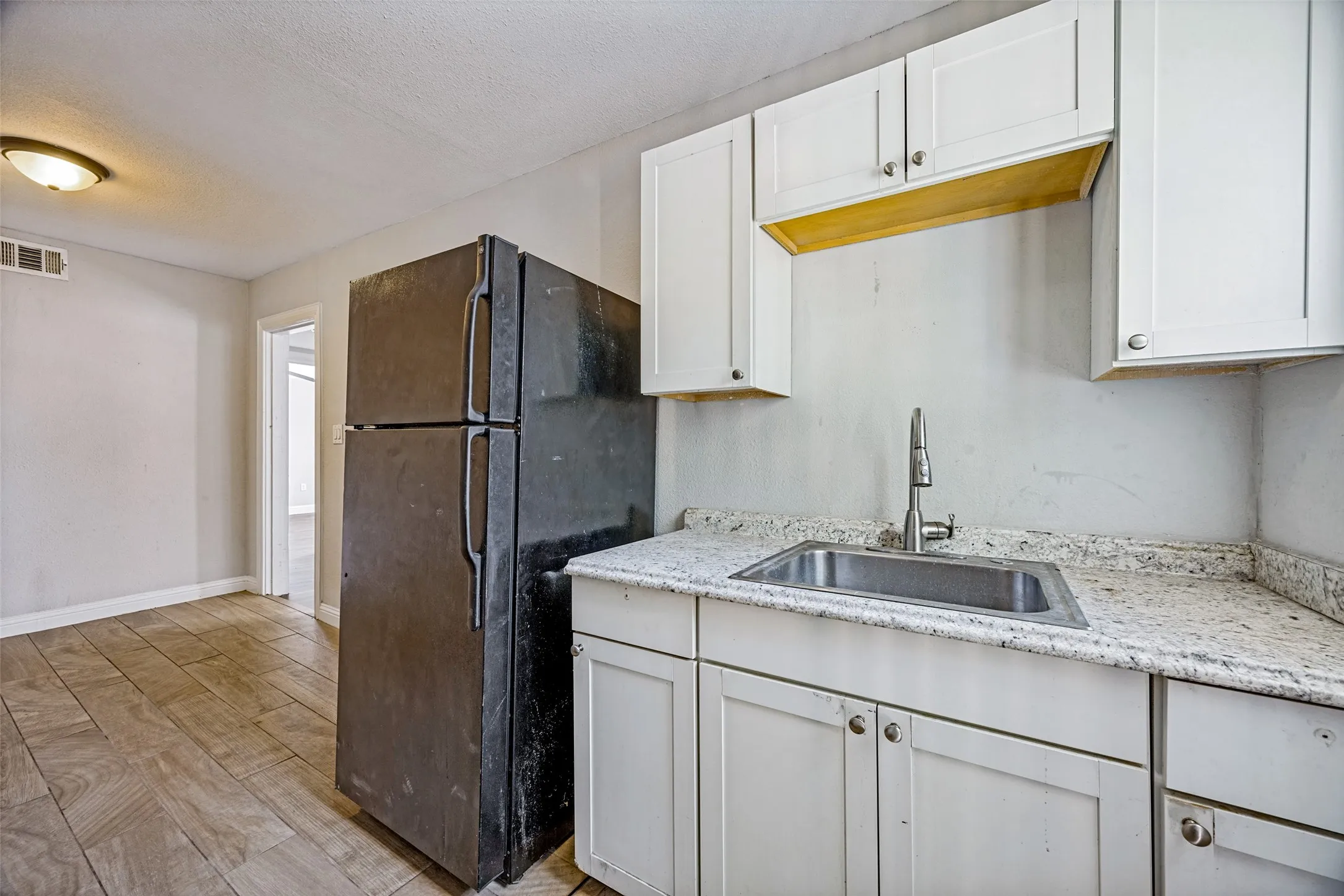 White cabinetry, stainless steel sink, contemporary faucet, light-toned countertops, and wood-finish flooring
