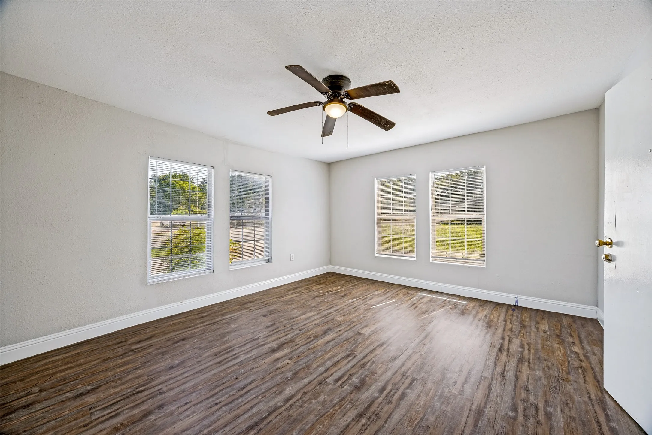 Wood-finish flooring, multiple windows providing ambient light, ceiling fan with integrated lighting, and white trim