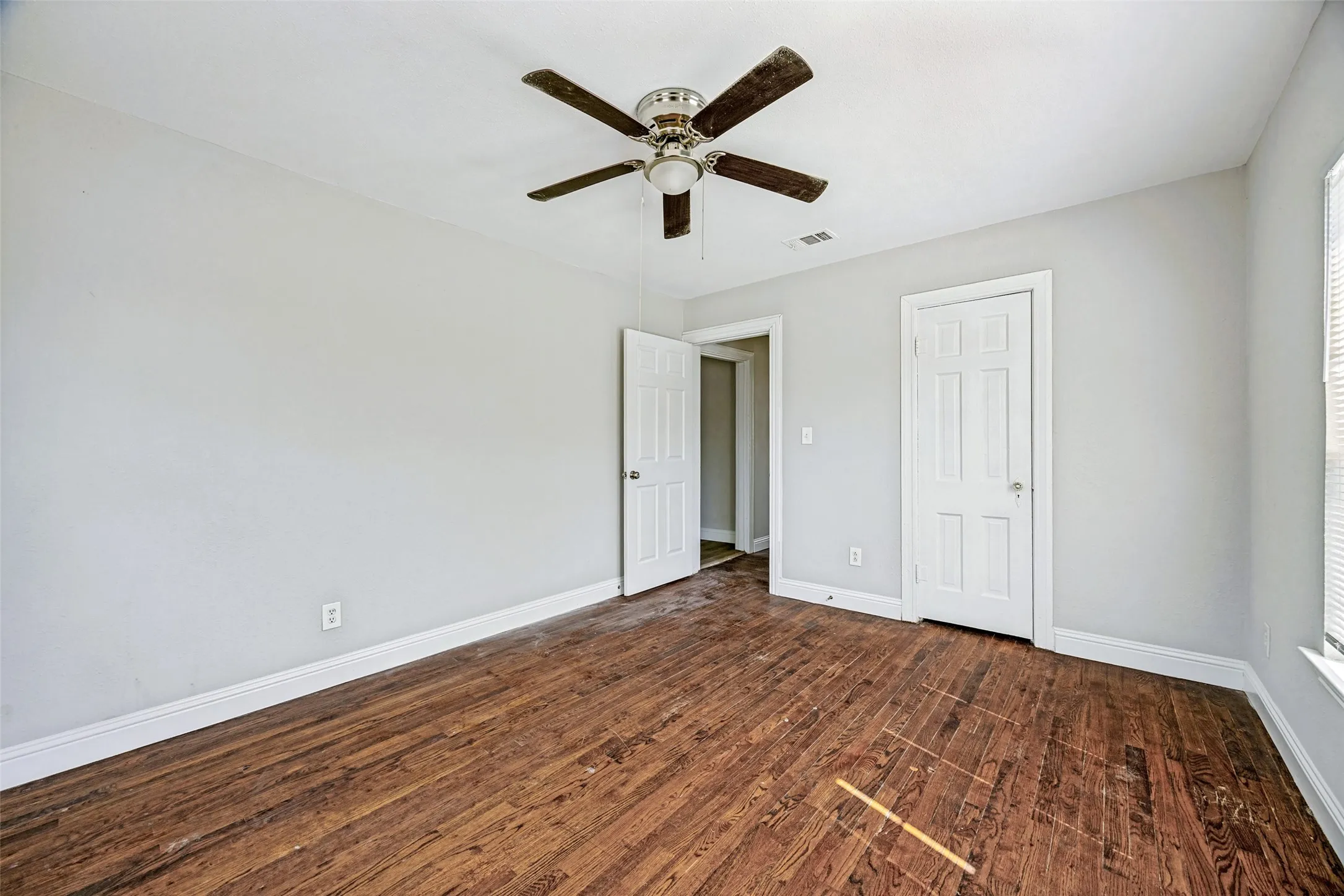 Wood-finish flooring, ceiling fan, white paneled doors, and natural light from the window