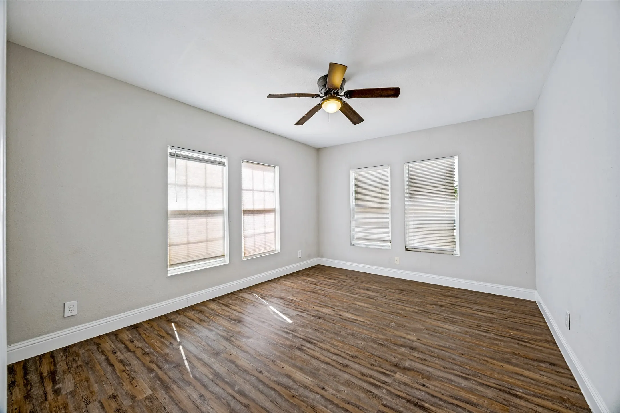 Wood-finish flooring, multiple windows with blinds, and a ceiling fan with integrated lighting