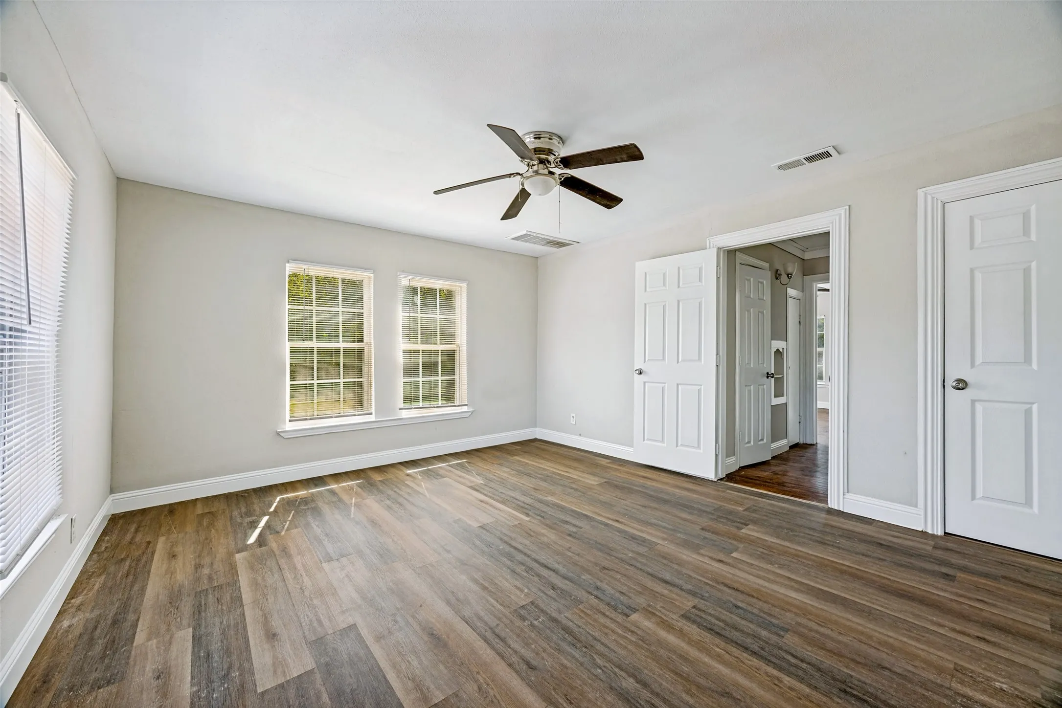 Spacious room featuring wood-finish flooring, two large windows, a ceiling fan, and crisp white trim throughout
