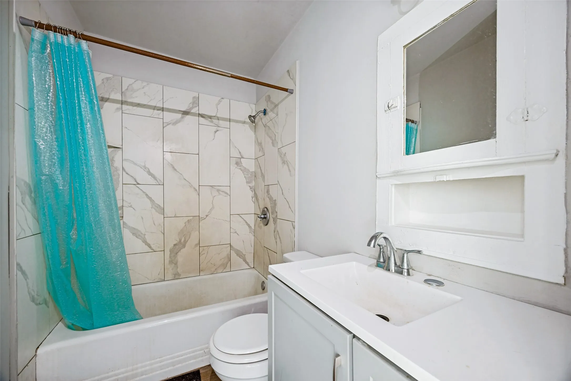 White bathtub with tiled shower surround, single vanity with integrated sink, chrome faucet, and recessed medicine cabinet