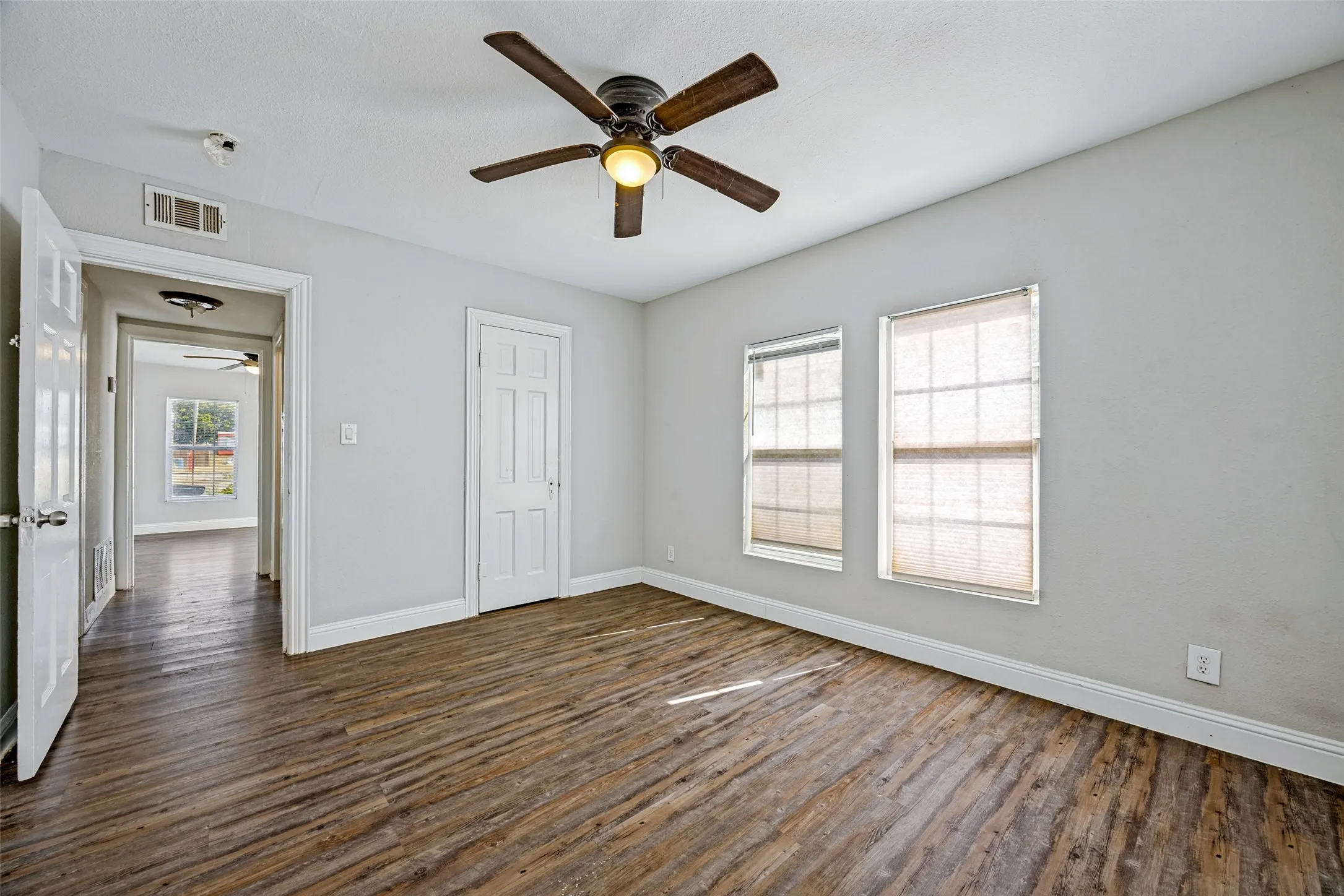 Wood-finish flooring, two windows with blinds, and a ceiling fan with integrated lighting