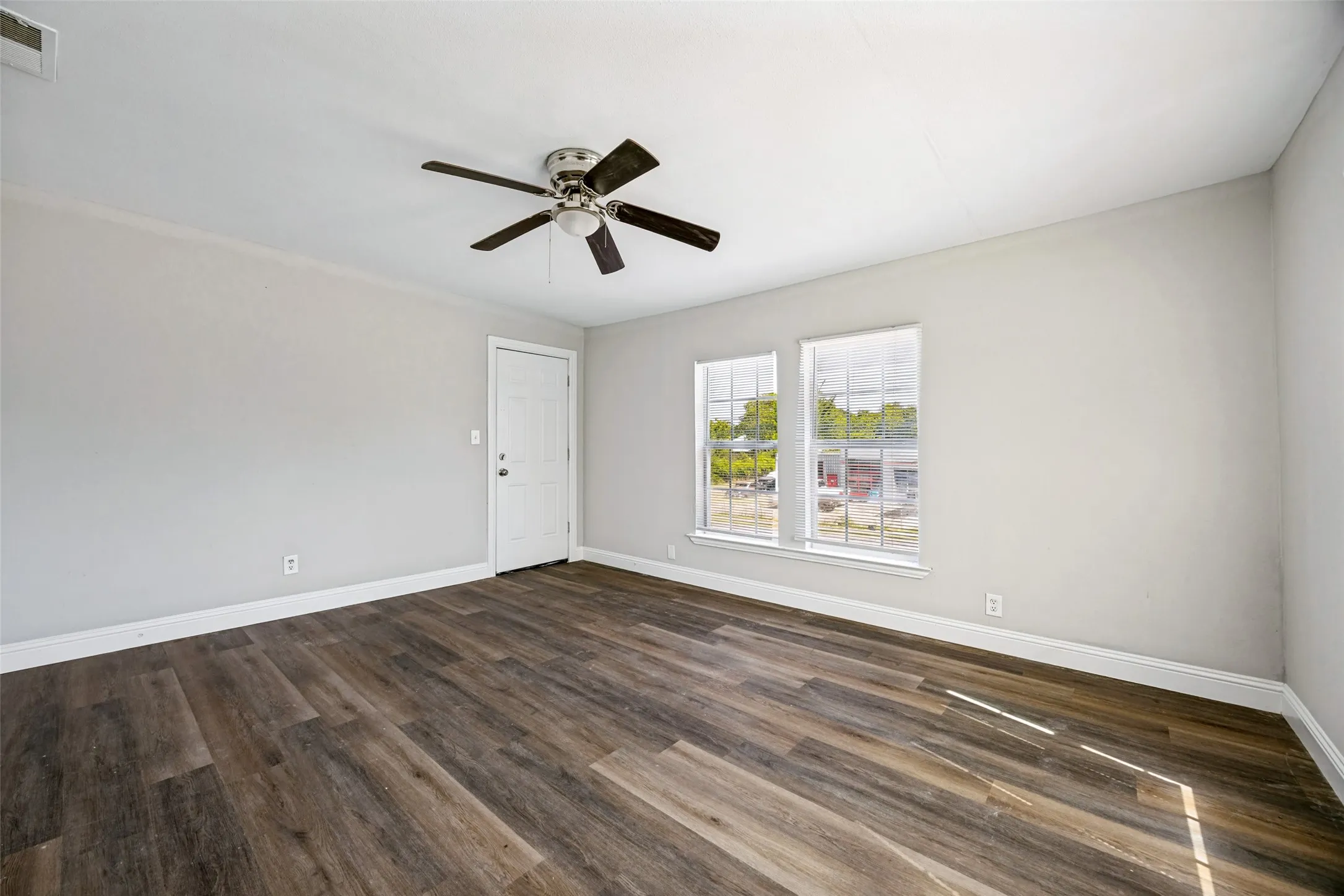 Wood-finish flooring with white baseboards, ceiling fan with light fixture, and two windows allowing natural light
