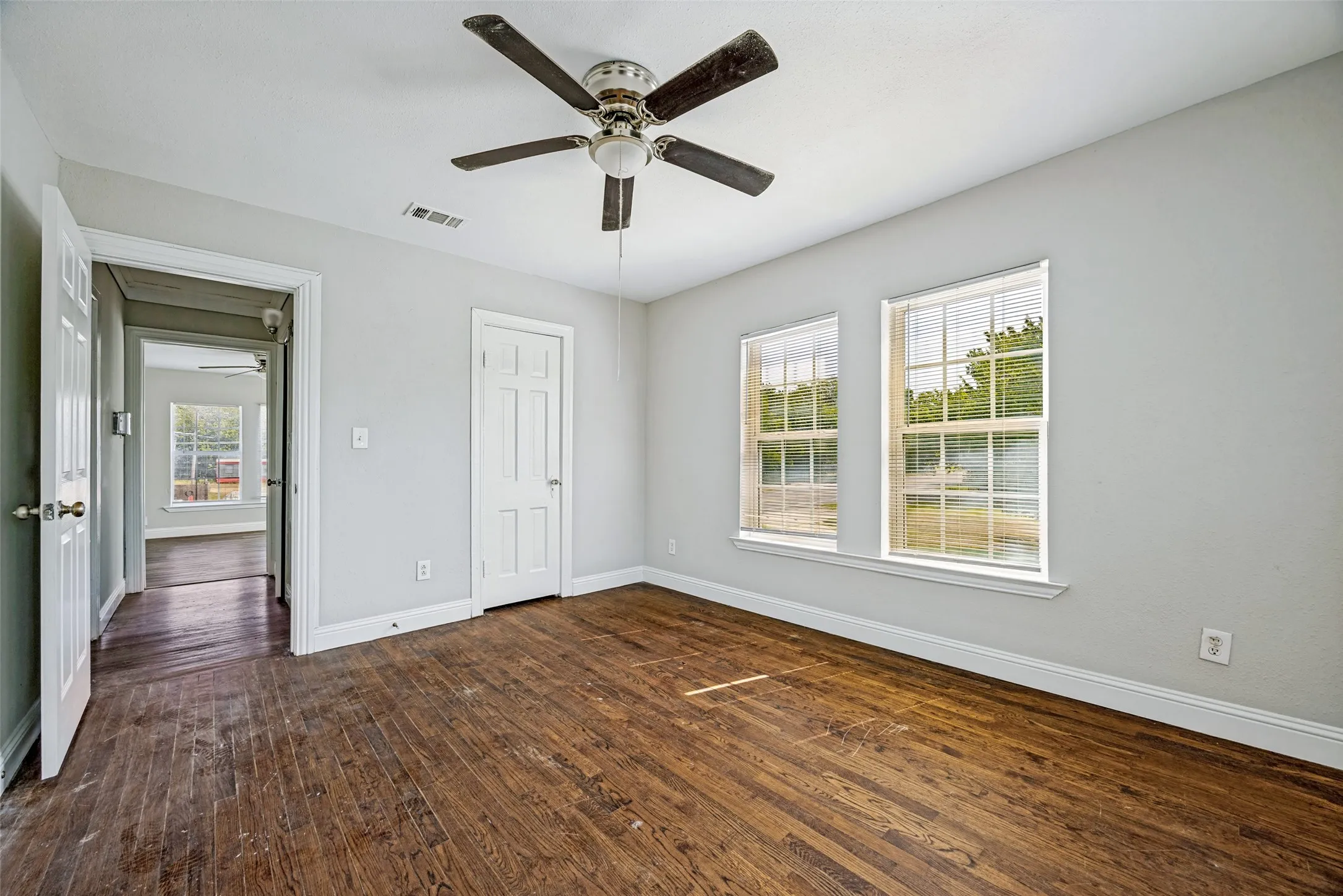 Hardwood flooring, two windows, ceiling fan, white paneled doors, and light-colored walls