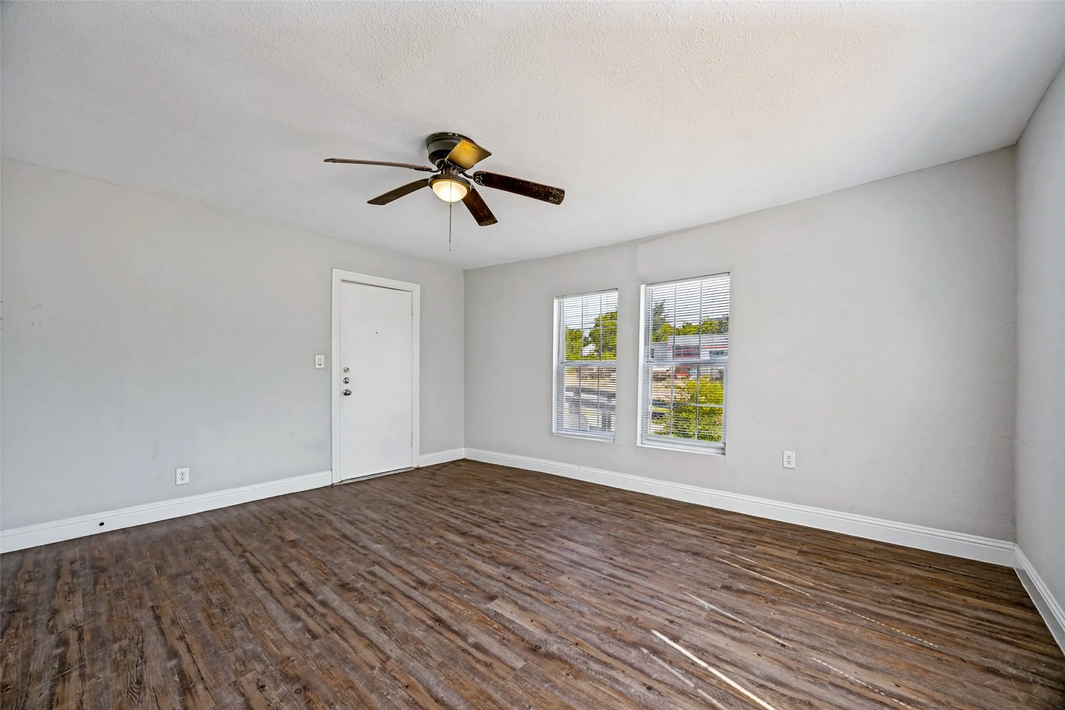 Wood-finish flooring, ceiling fan with integrated lighting, multiple windows, and a white entry door