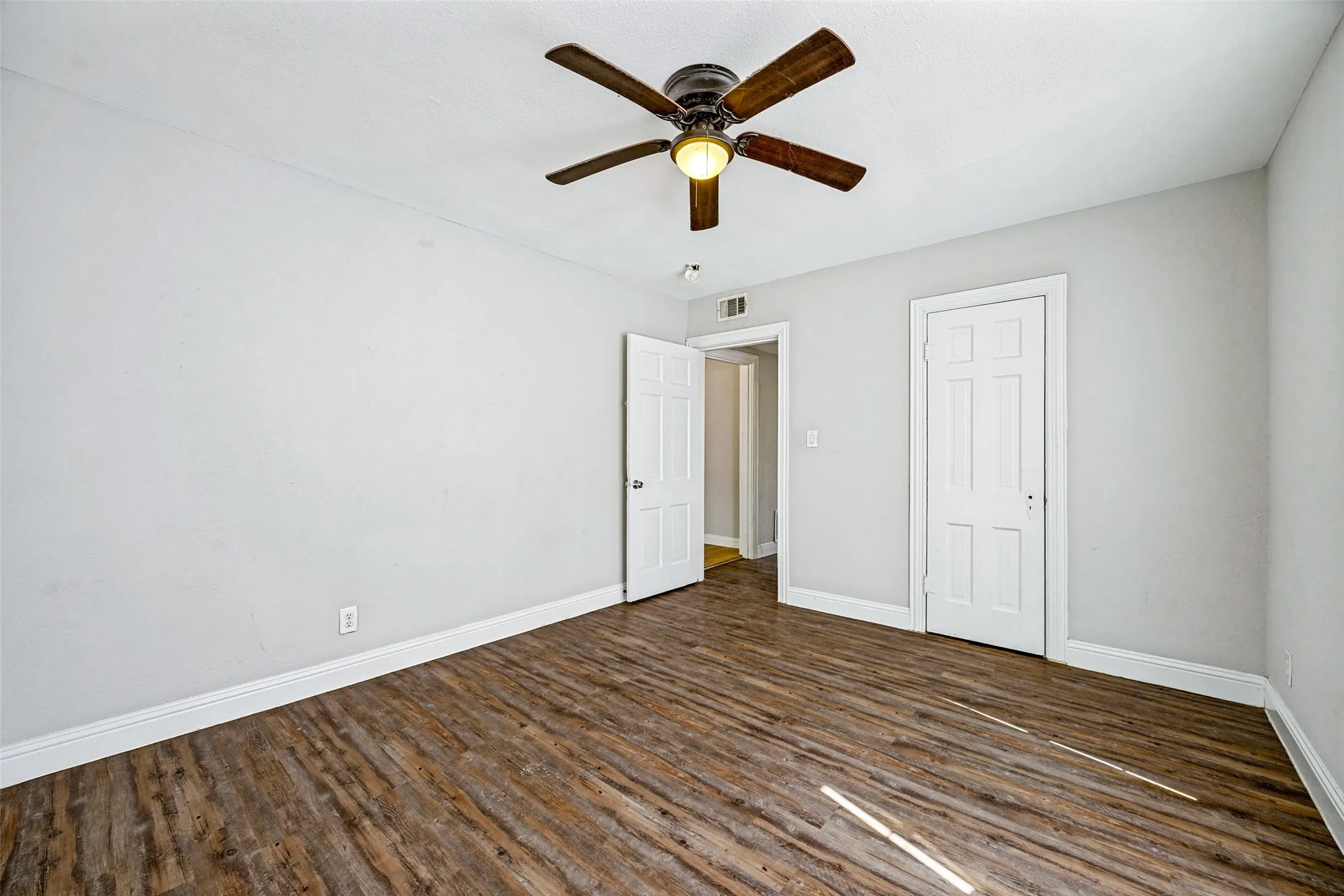 Wood-finish flooring, white walls, and a ceiling fan with integrated lighting