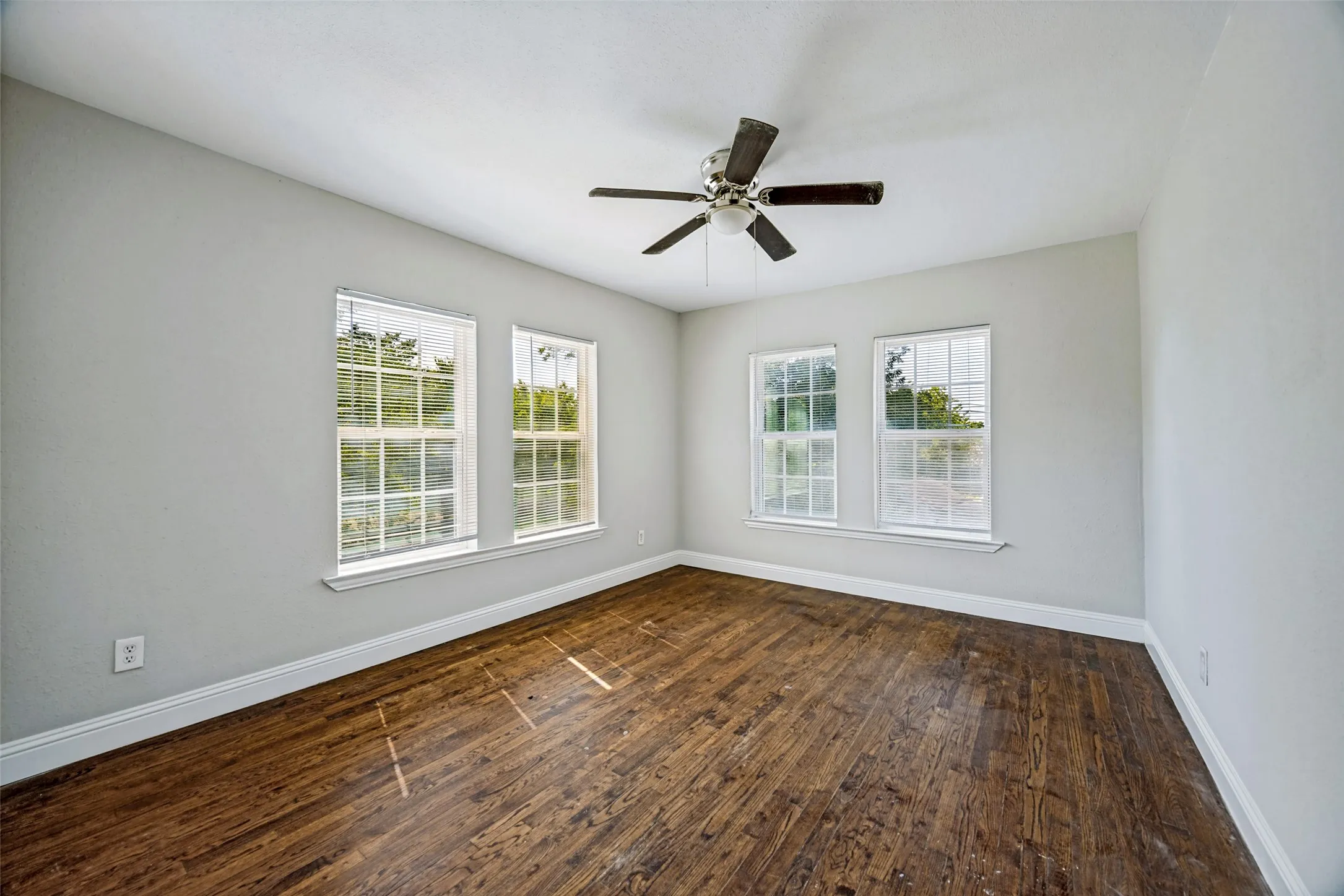 Wood-finish flooring, multiple windows with natural light, ceiling fan, and crisp white trim