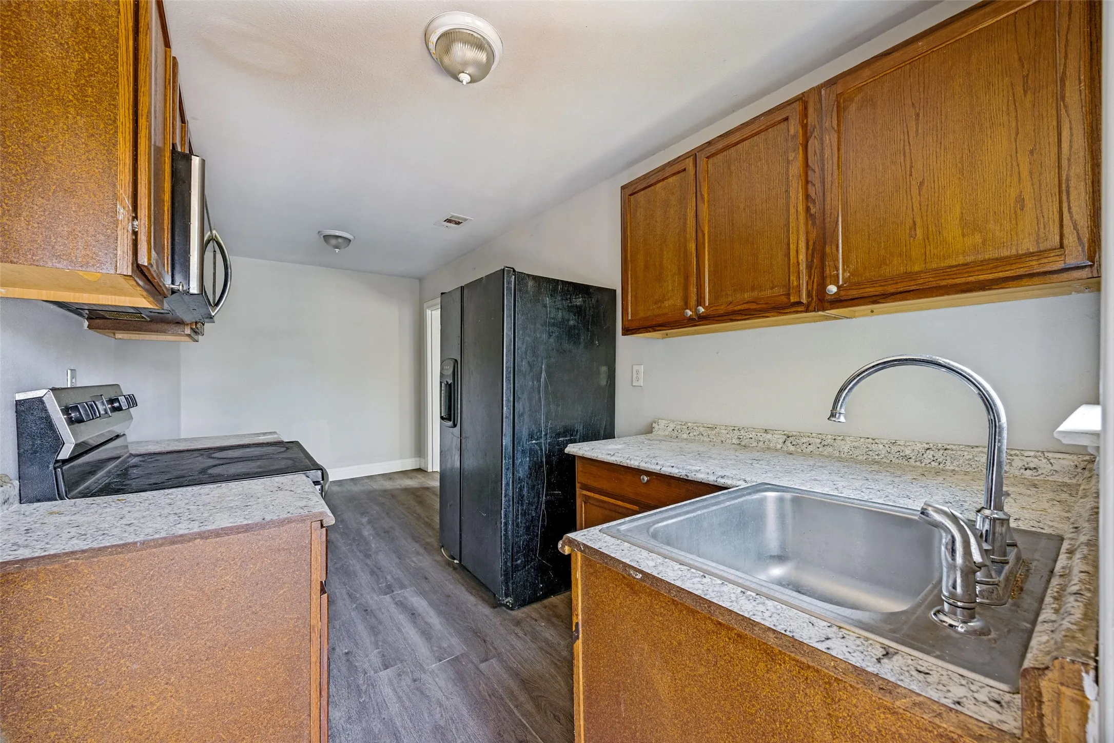 Kitchen featuring wood cabinetry, laminate countertops, stainless steel sink with gooseneck faucet, and wood-finish flooring