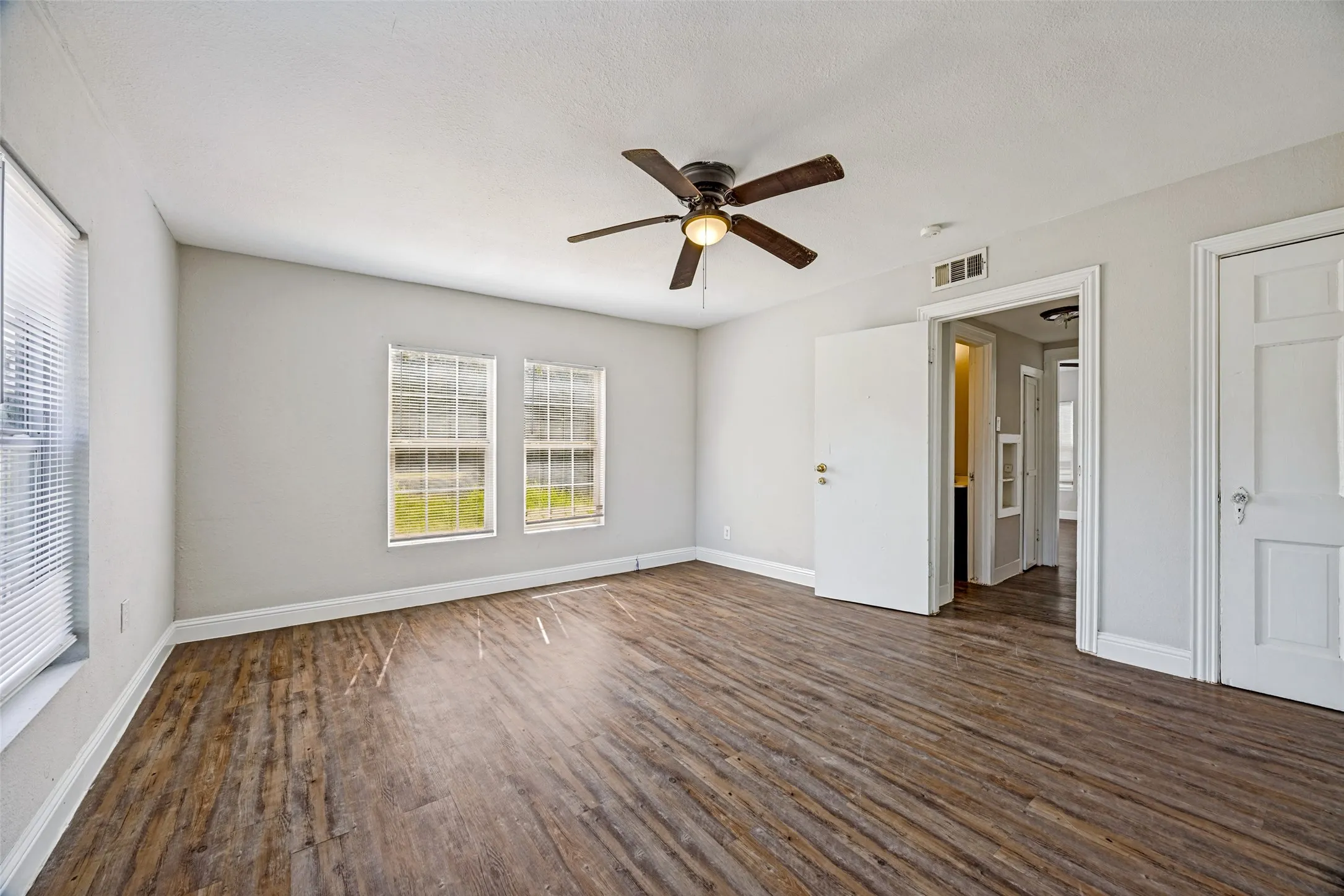 Spacious interior featuring wood-finish flooring, light gray walls, white trim, and a ceiling fan with integrated lighting