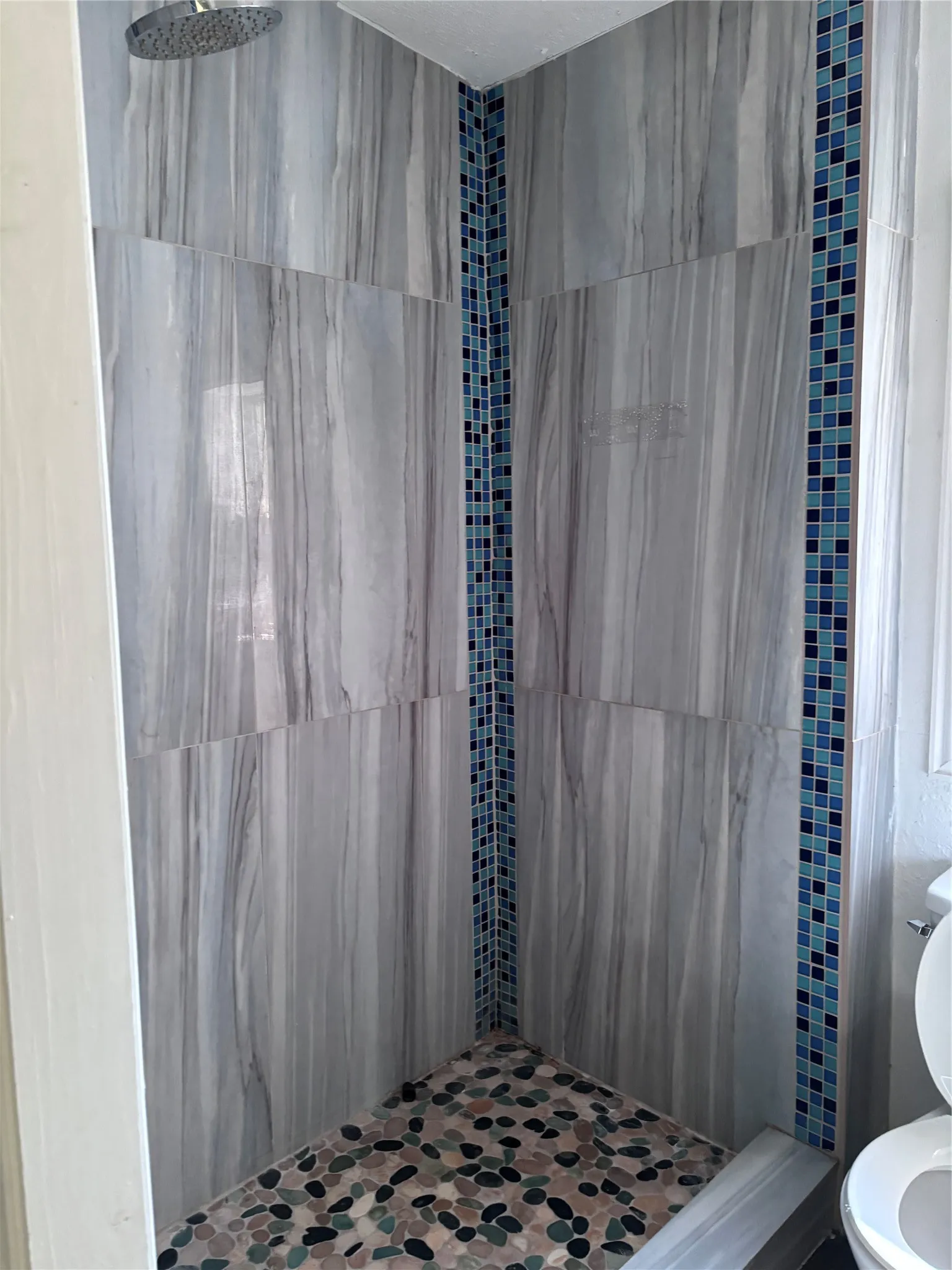 Tiled shower with a rainfall shower head, stone pebble flooring, and blue mosaic tile accents