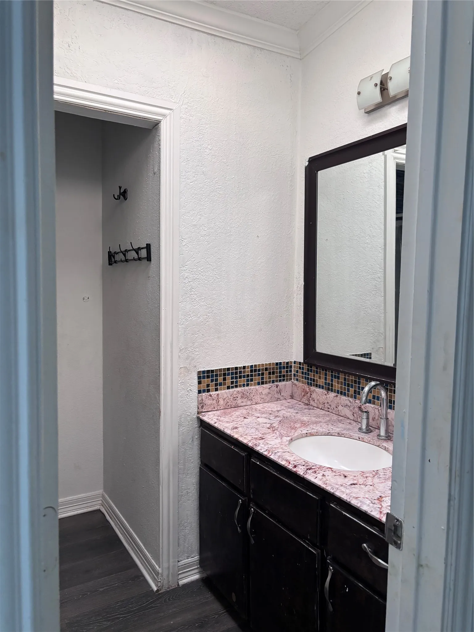 Vanity with a pink marble-look countertop, integrated white sink, mosaic tile backsplash, and dark wood-finish cabinetry