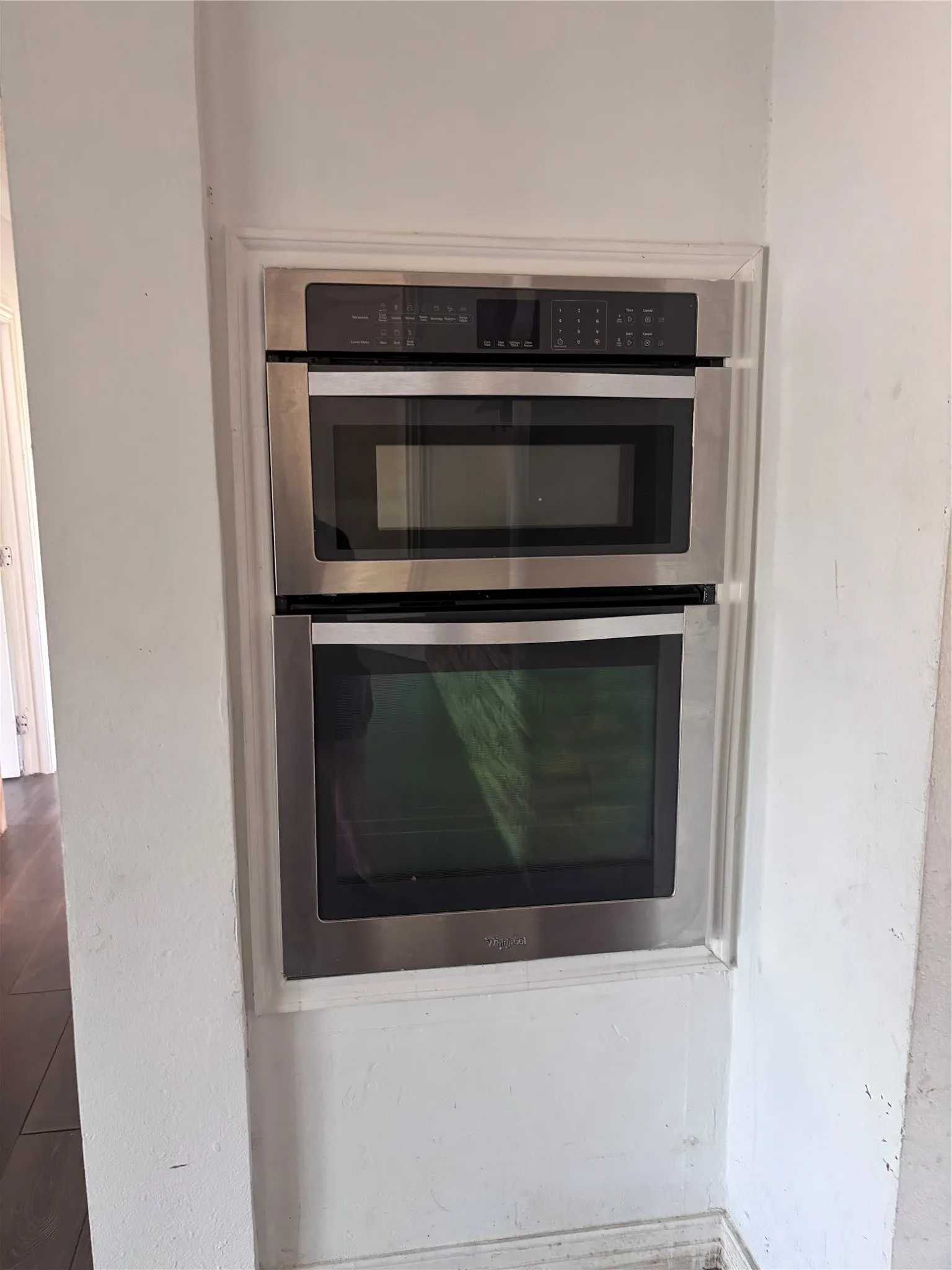 Built-in stainless steel appliances including a microwave oven and convection oven with black trim and control panels, integrated into a custom cabinetry alcove with white painted finish and clean architectural framing