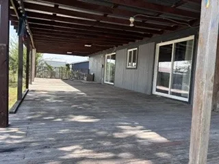 Expansive covered porch with a wood-finish deck, exposed beam ceiling, and multiple sliding glass doors