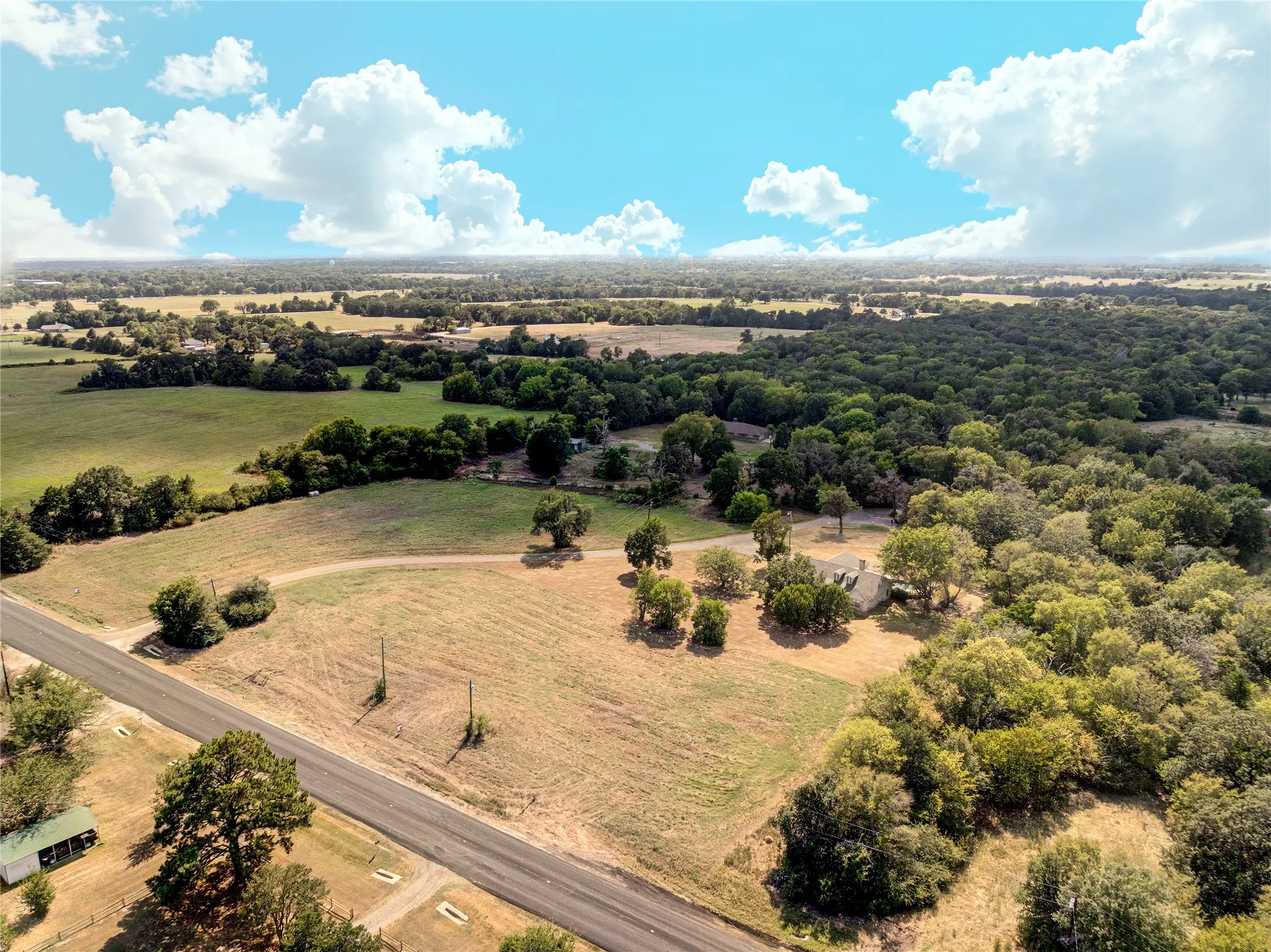 Expansive acreage featuring a single-story residence, mature trees, and a paved road