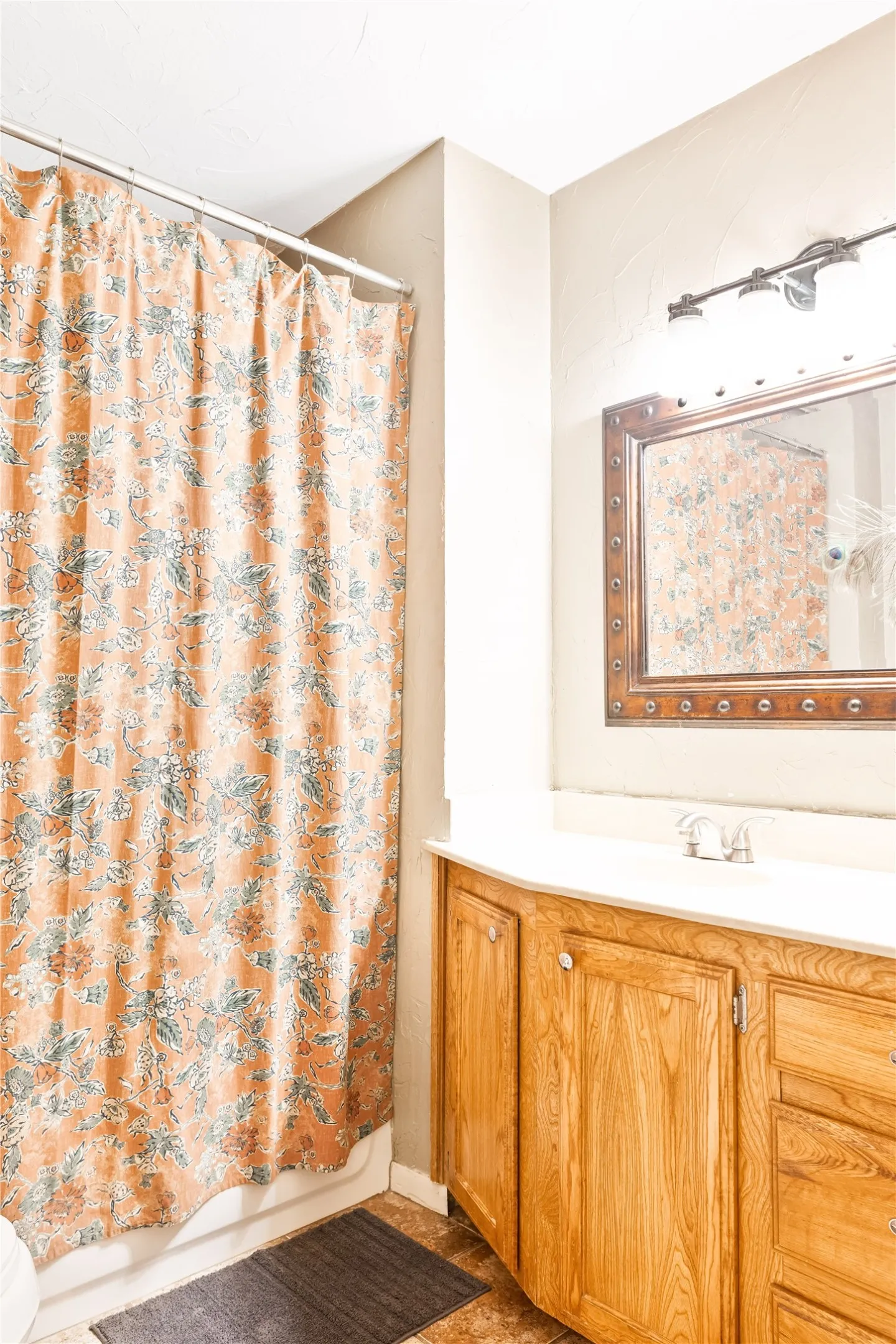 Built-in wood-finish vanity with a white countertop and integrated sink, framed mirror with decorative trim, and a wall-mounted light fixture