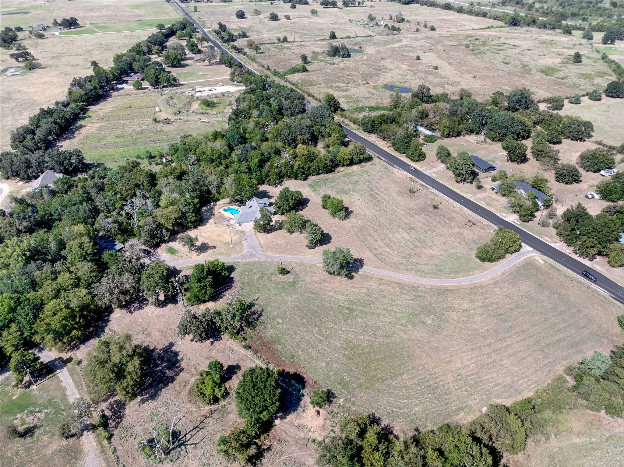 Expansive rural property featuring a main residence, an in-ground pool, a paved road, and a substantial tree line