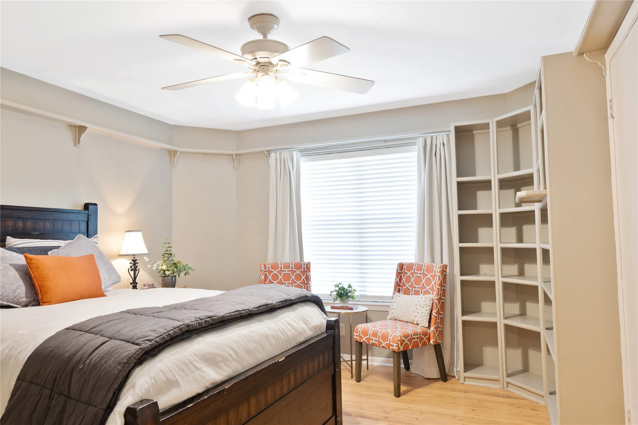 Recessed window with blinds, wood-finish flooring, ceiling fan with integrated lighting, built-in shelving, and crown molding