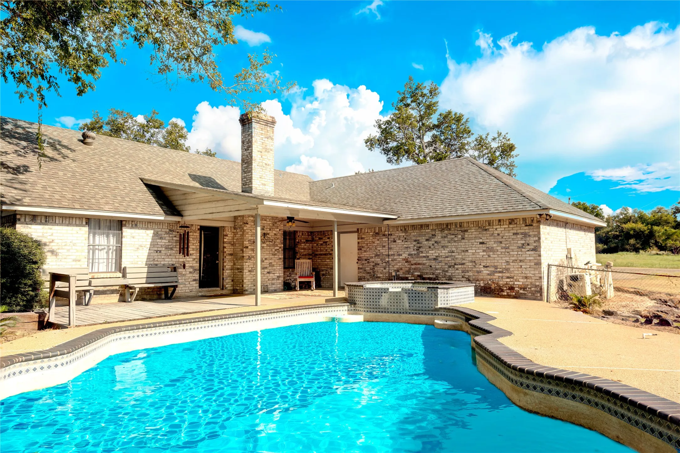 Brick exterior with a gabled roofline, featuring a covered patio, an in-ground swimming pool, and an integrated spa
