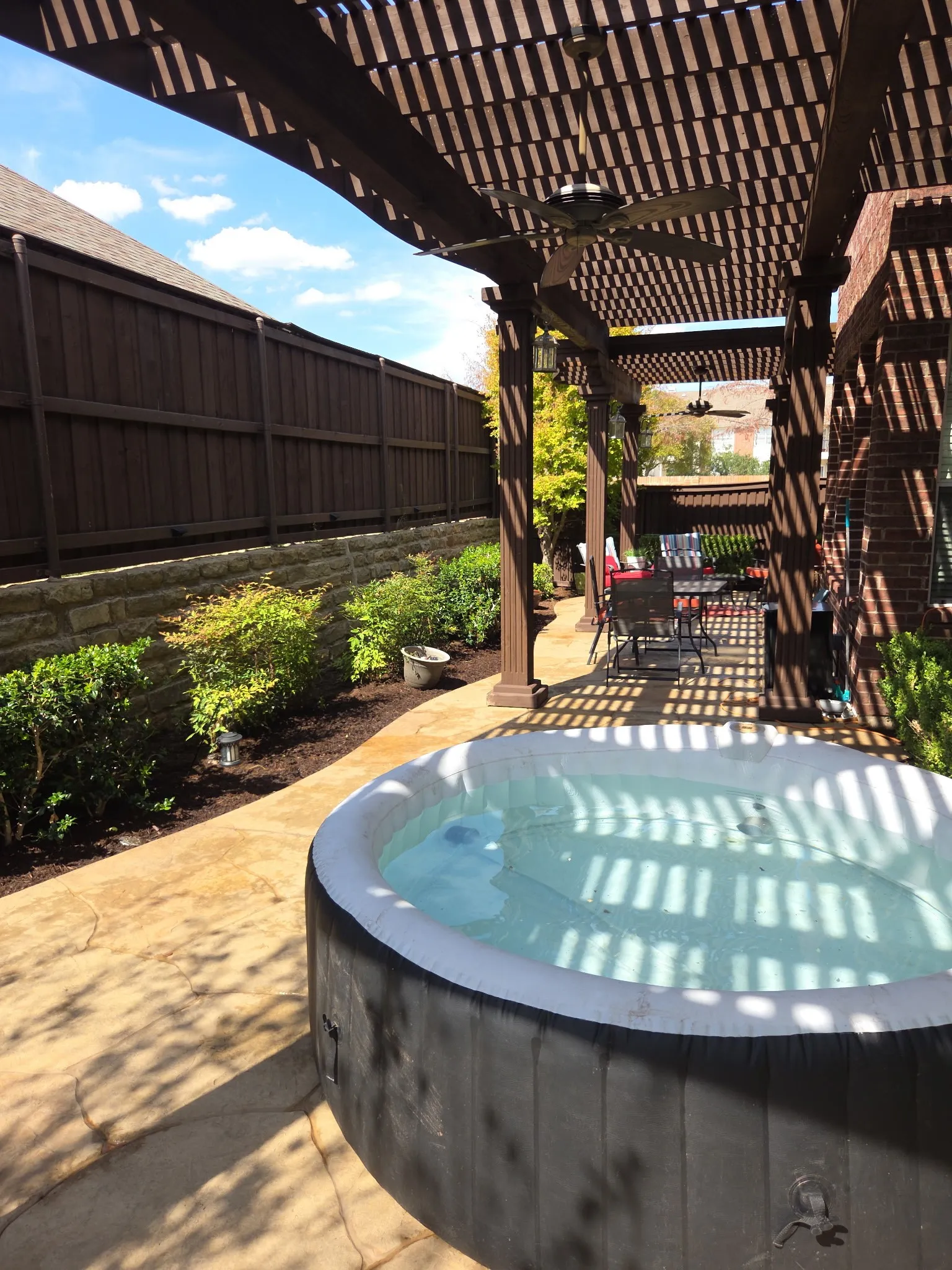 Patio with a pergola, two ceiling fans, a hot tub, and a stone retaining wall with plantings