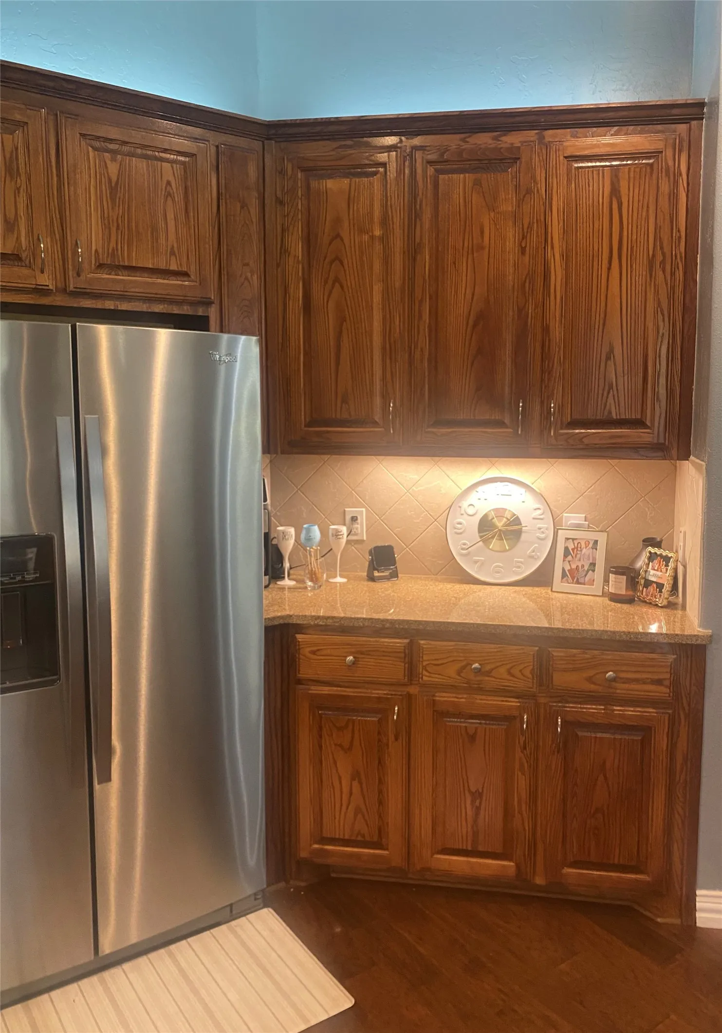 Full-height wood cabinetry with crown molding, natural stone countertop, diagonal tile backsplash, and wood-finish flooring