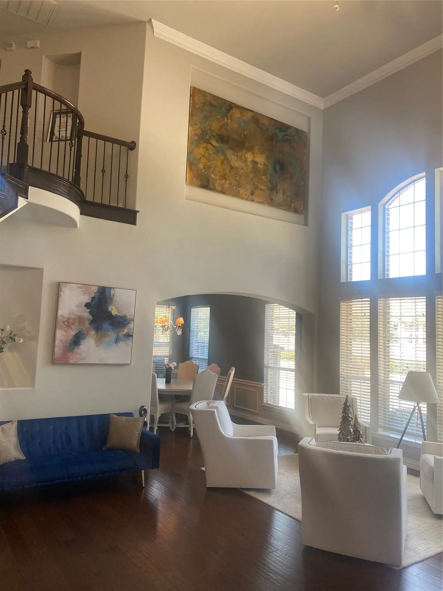 Two-story living area featuring dark wood-finish flooring, a grand curved staircase with dark wood and wrought iron balusters, and a recessed art niche