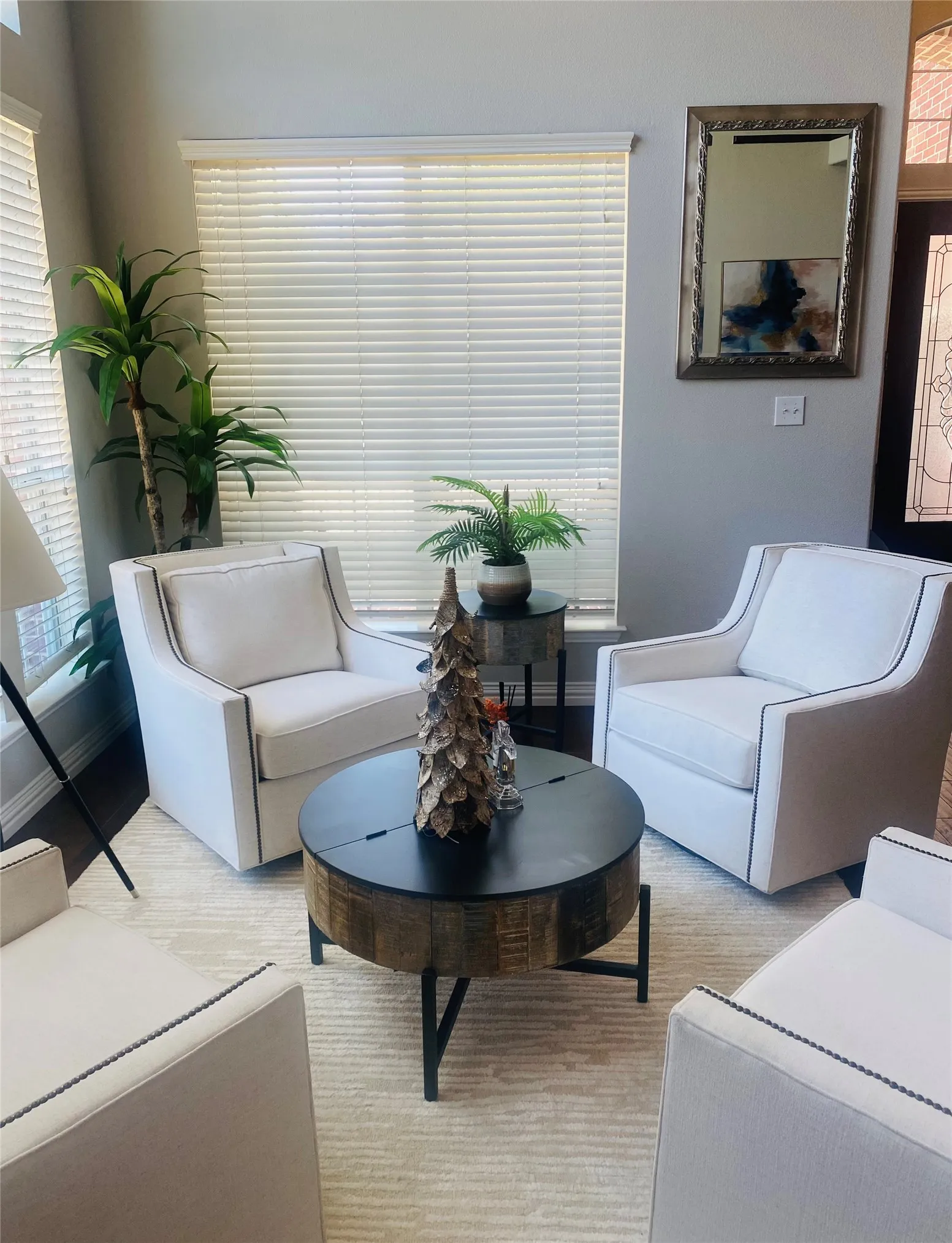 Light-filled formal sitting area with multiple windows, neutral wall tones, and dark wood-finish flooring