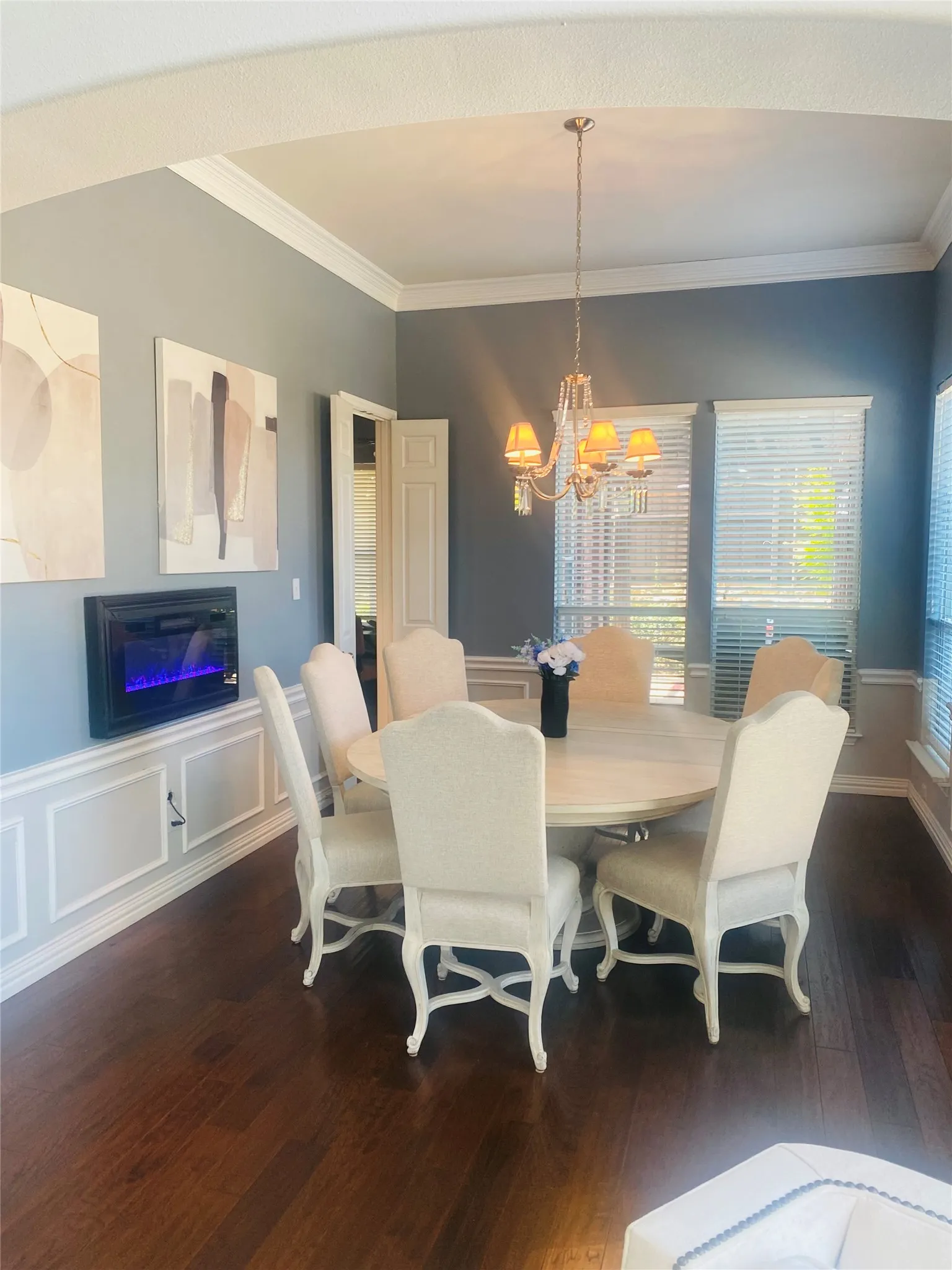 Wood-finish flooring, crown molding, chair rail molding, built-in electric fireplace, and a decorative chandelier