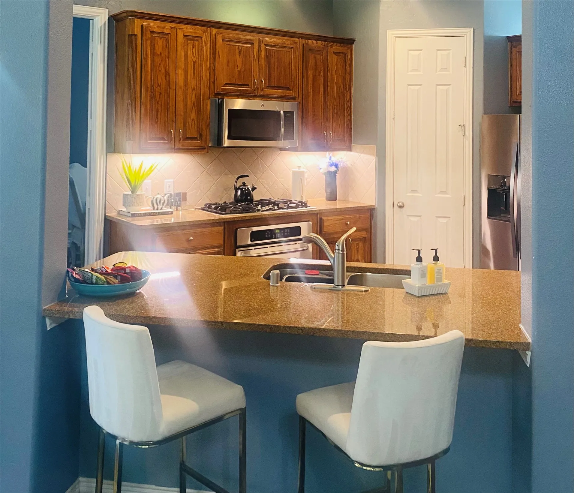 Kitchen featuring wood cabinetry, stainless steel appliances, a tile backsplash, and a breakfast bar with stone countertops