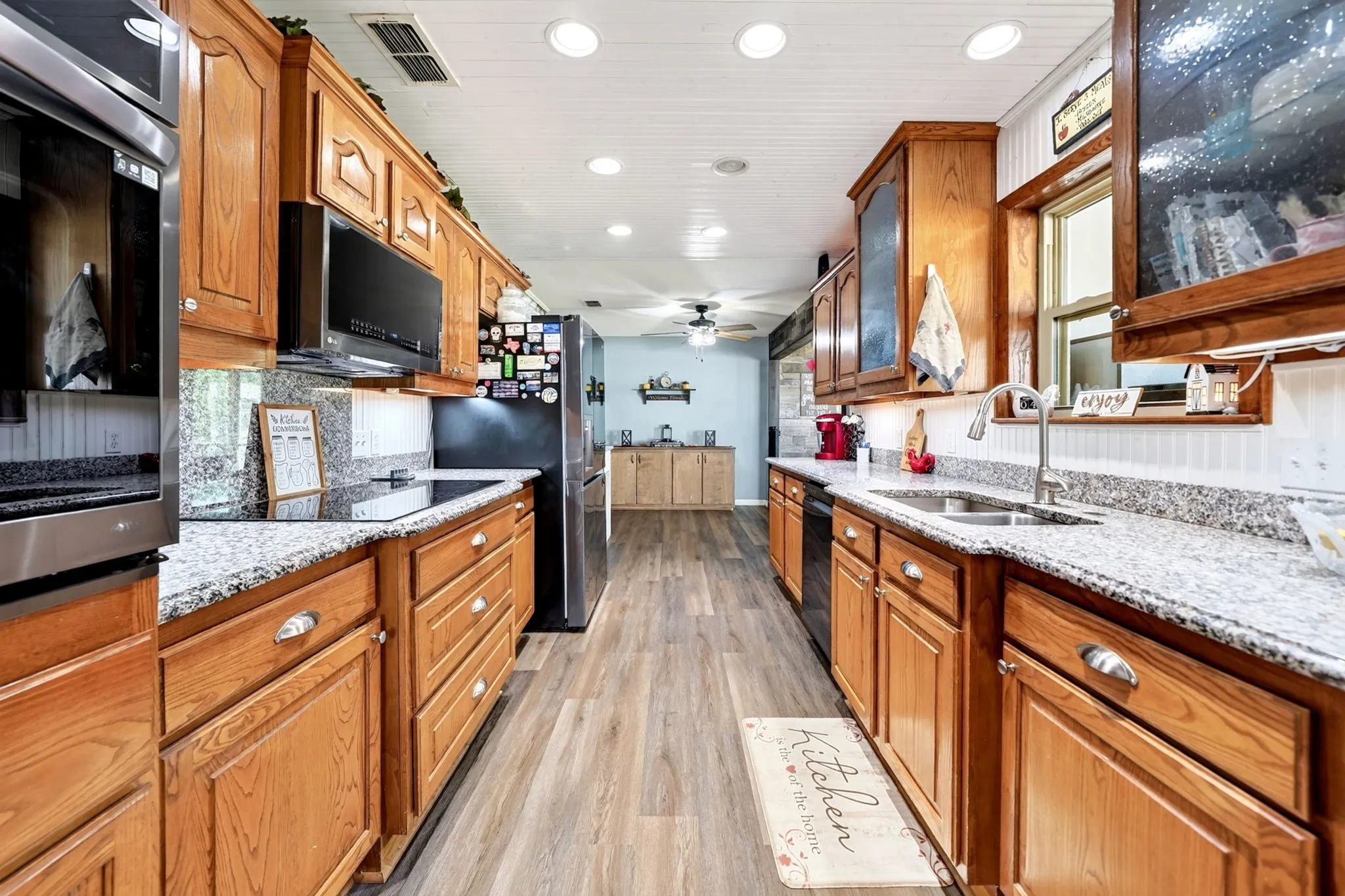 Galley kitchen featuring wood-finish cabinetry, speckled countertops, stainless steel double basin sink, and recessed lighting