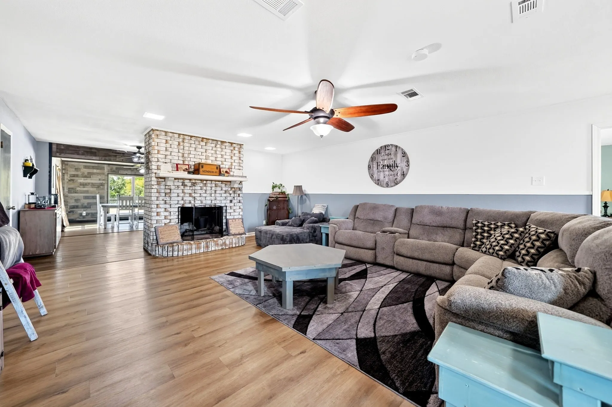 Living area featuring wood-finish flooring, a brick fireplace, a ceiling fan with integrated lighting, and recessed ceiling lights