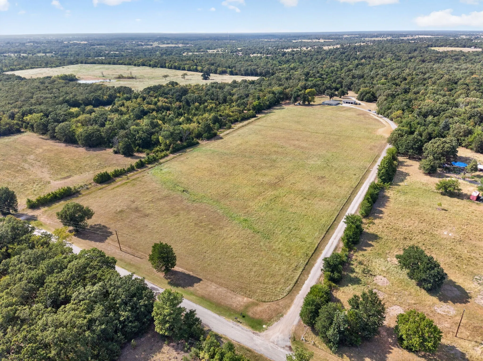 Expansive open field bordered by mature trees and a gravel road