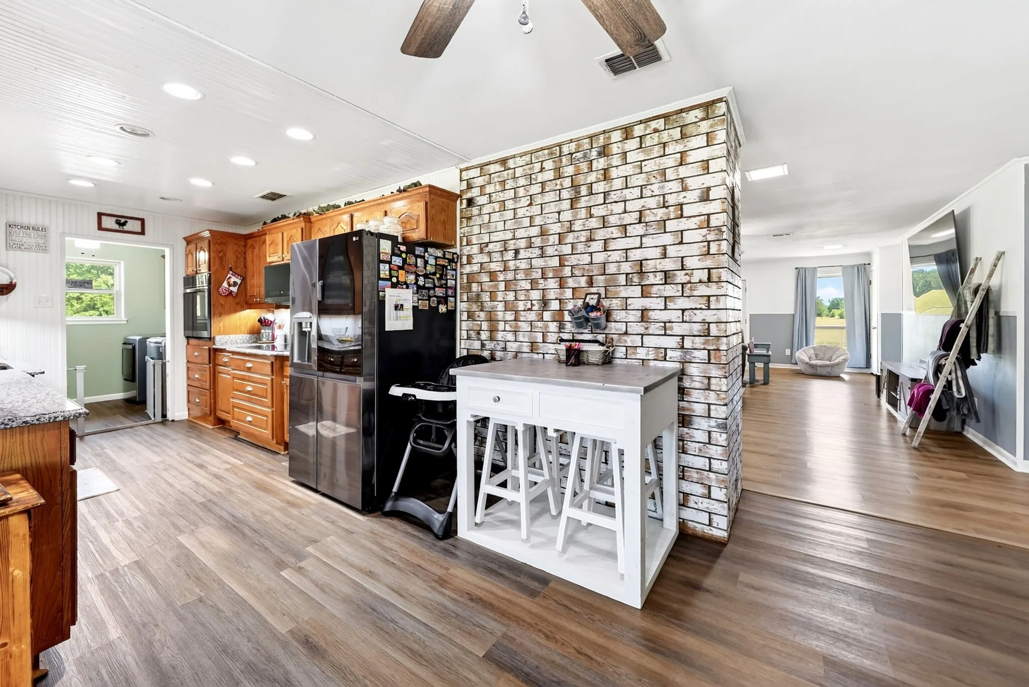 Kitchen featuring wood cabinetry, granite-style countertops, wood-finish flooring, and a whitewashed brick accent wall