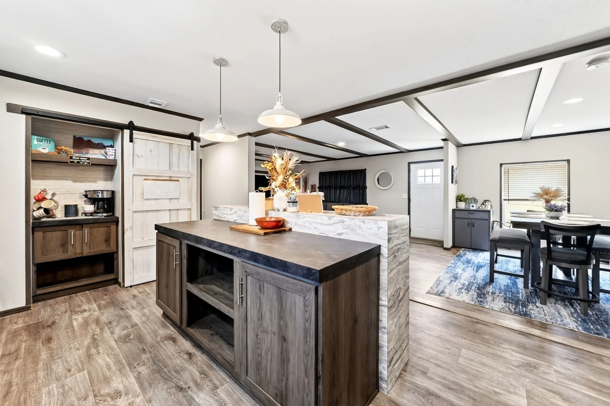 Open-concept living space with wood-finish flooring, a kitchen island with integrated storage, and exposed beam ceiling details