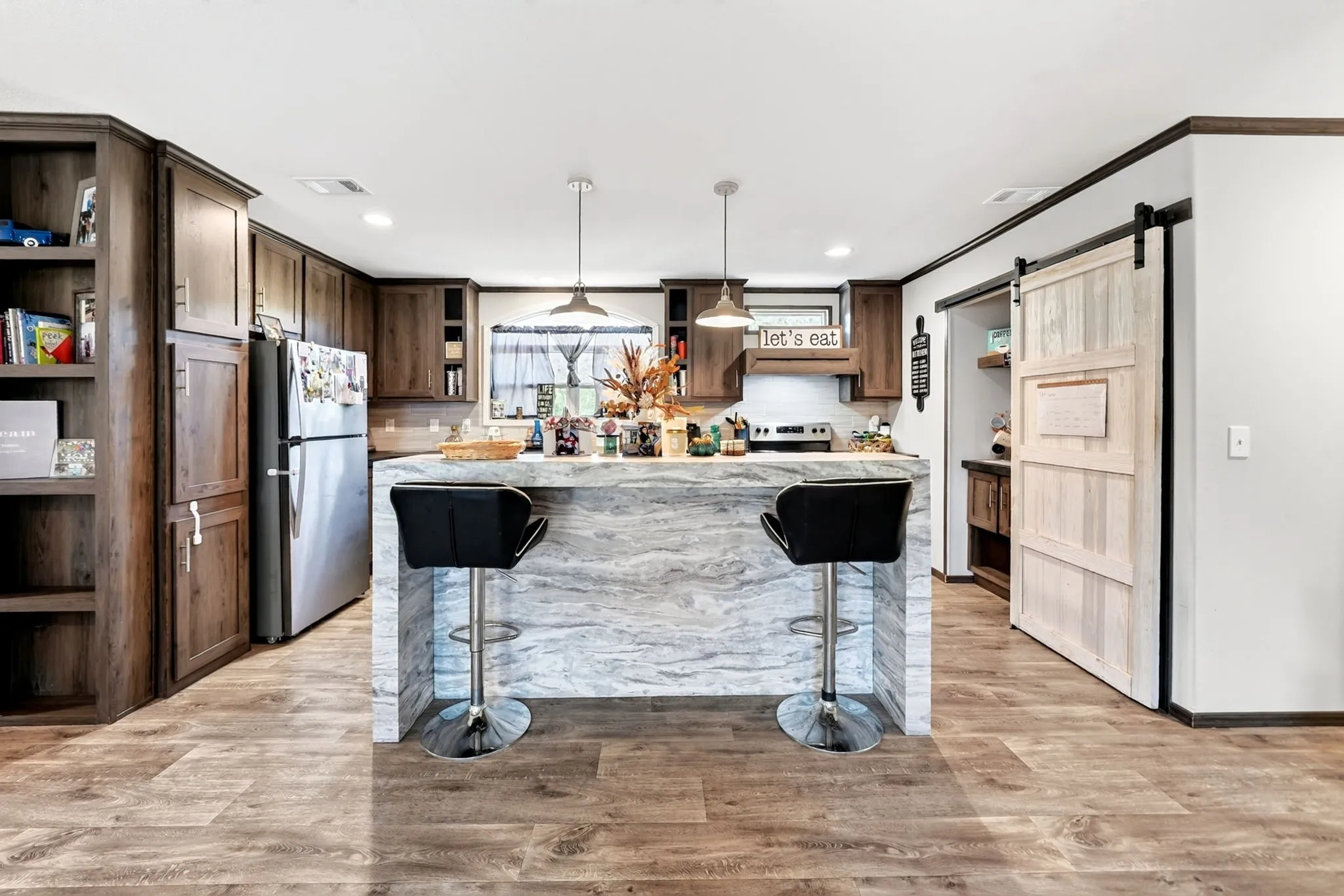 Wood-finish flooring, built-in shelving, stainless steel refrigerator, kitchen island with counter seating, and a sliding barn door