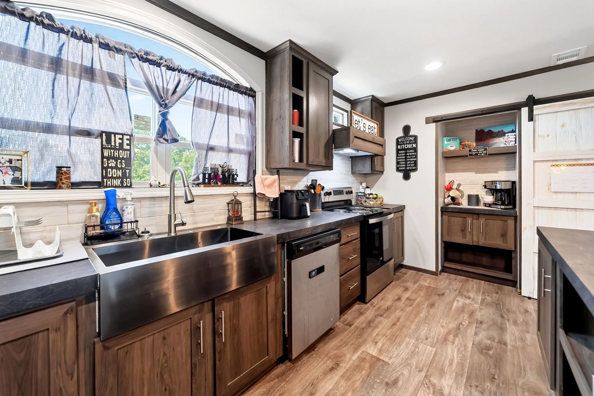 Kitchen featuring wood-finish flooring, dark countertops, a stainless steel farmhouse sink, and a pantry with a barn door