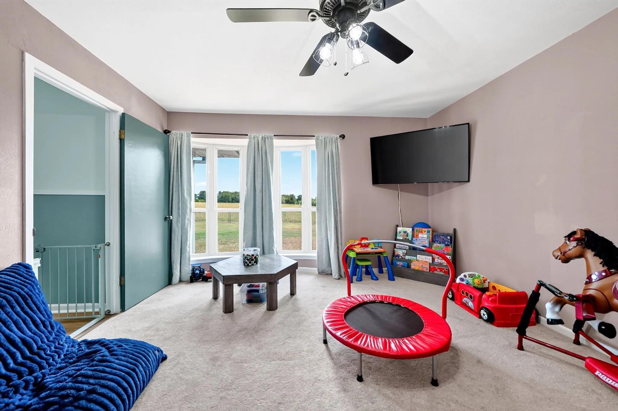Carpeted room with a ceiling fan, bay windows, and a wall-mounted television